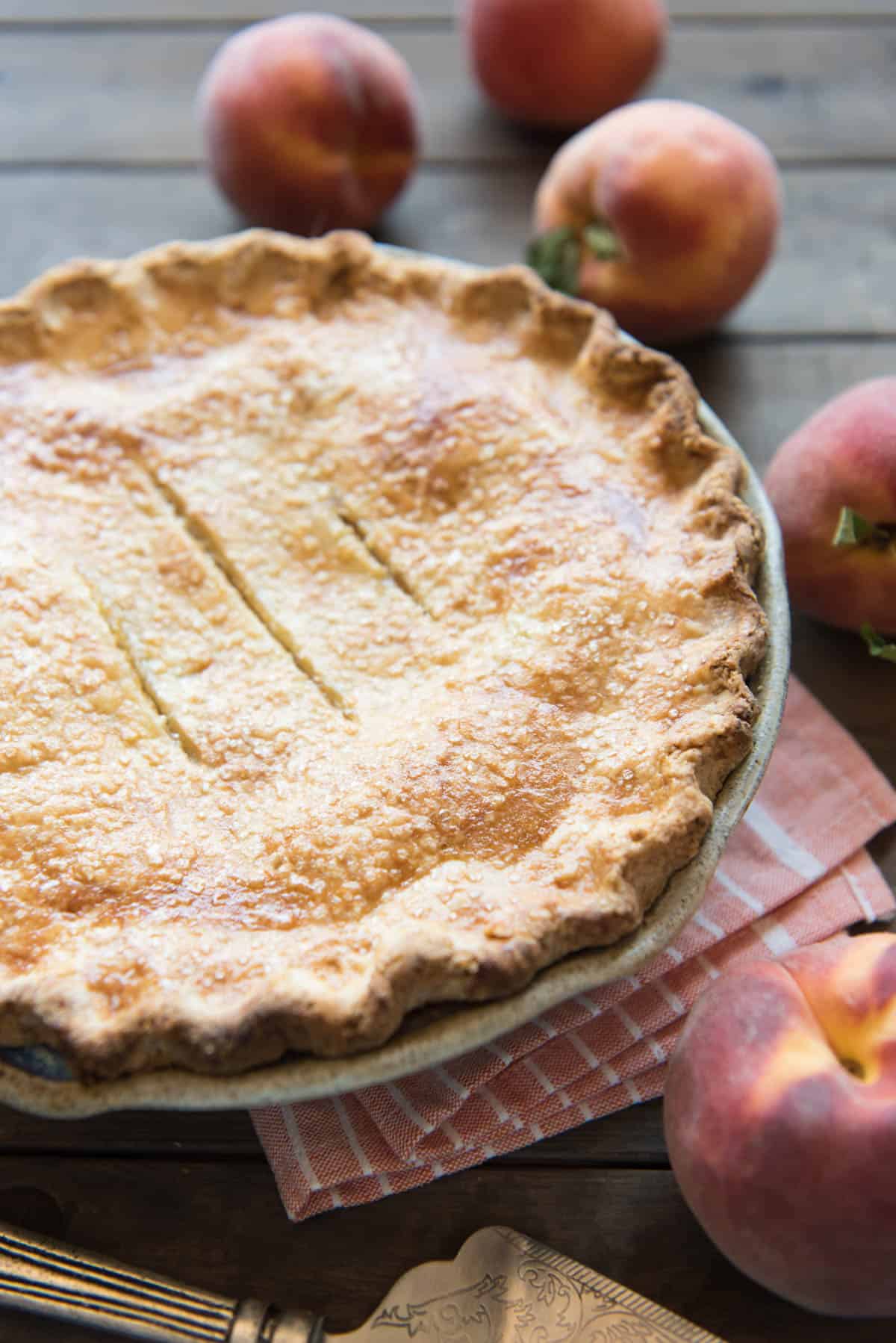 An image of a peach pie with fresh peaches in the background.