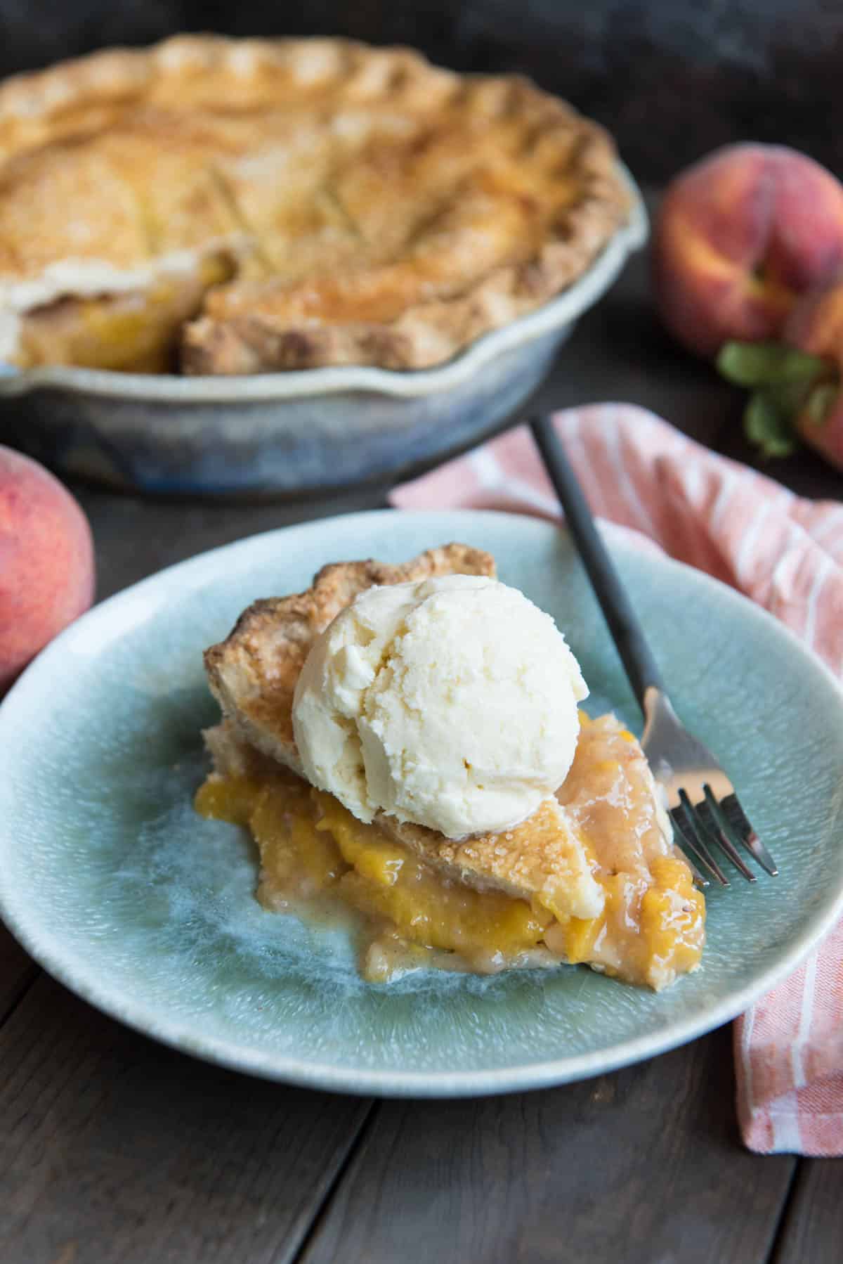 A slice of southern peach pie on a blue plate with ice cream on top and a fork to the side.