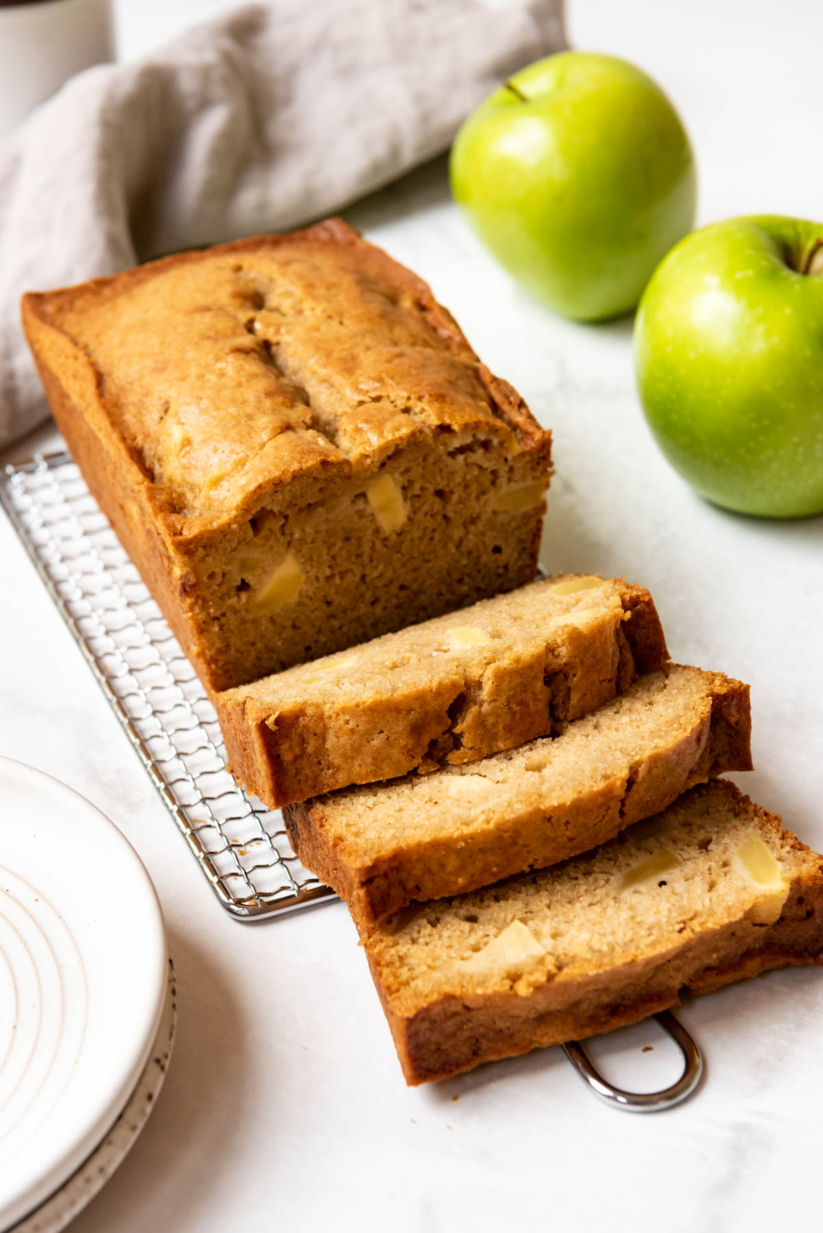 A partially sliced loaf of apple quick bread next to green apples.