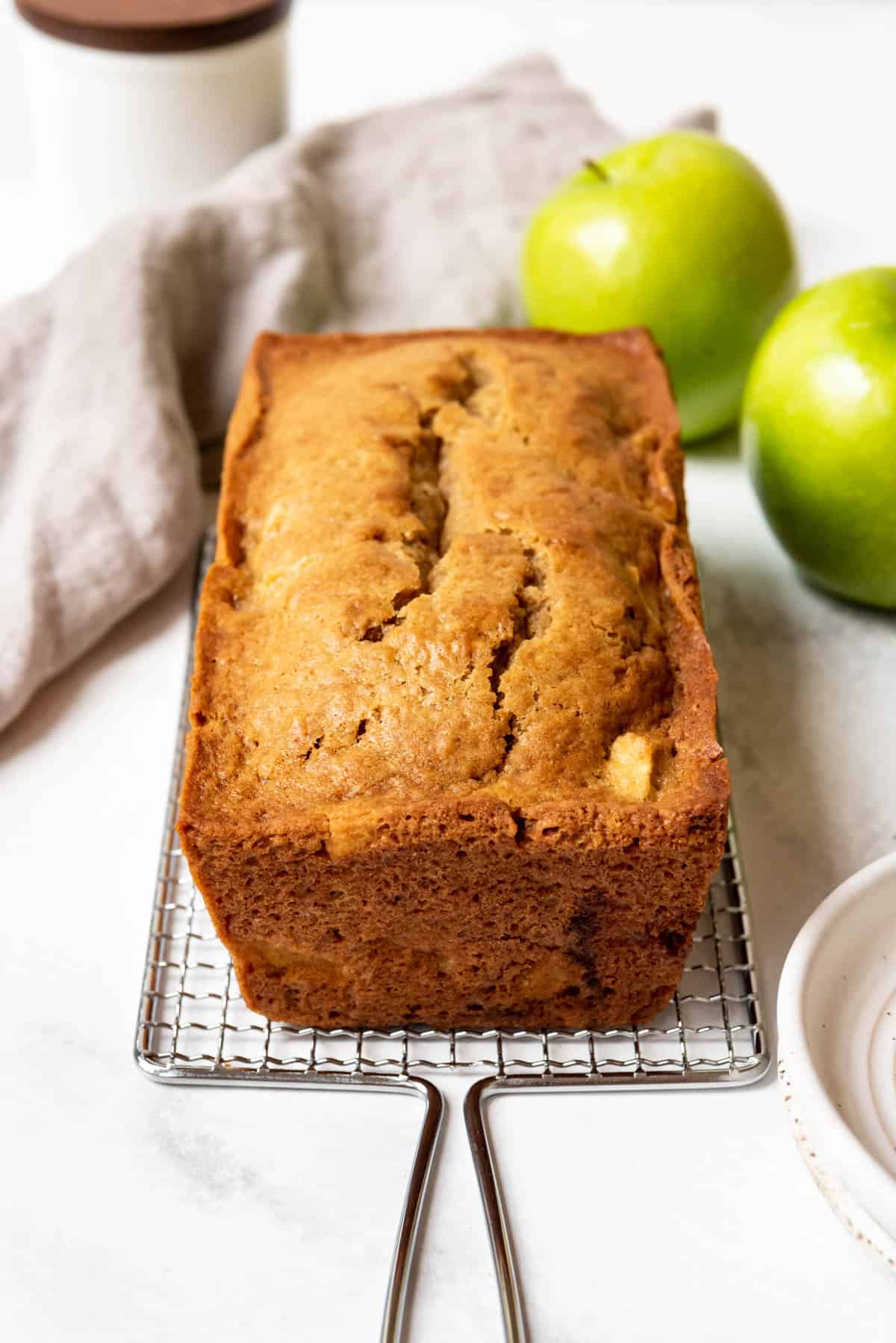 A loaf of apple ginger quick bread on a metal cooling rack.