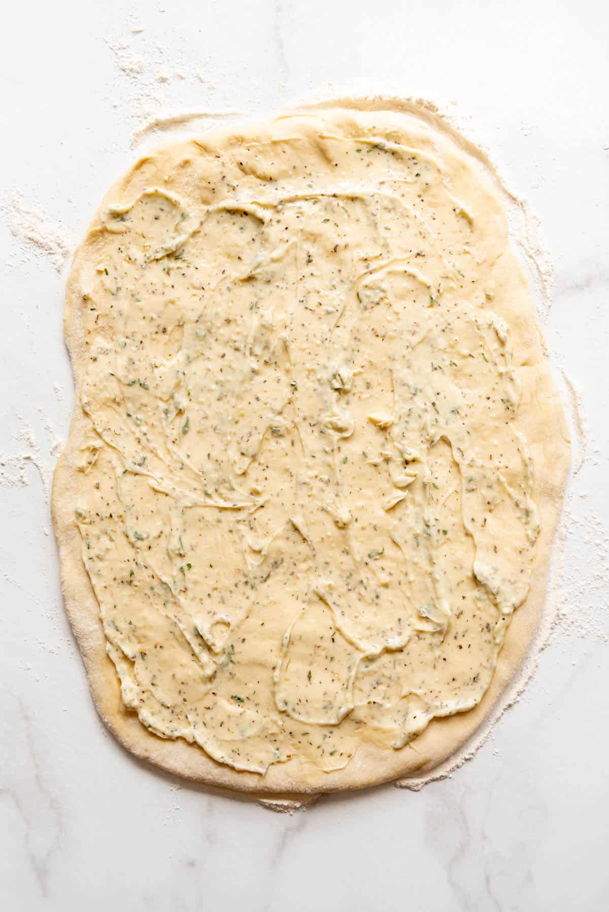 Softened garlic butter spread onto roll dough.