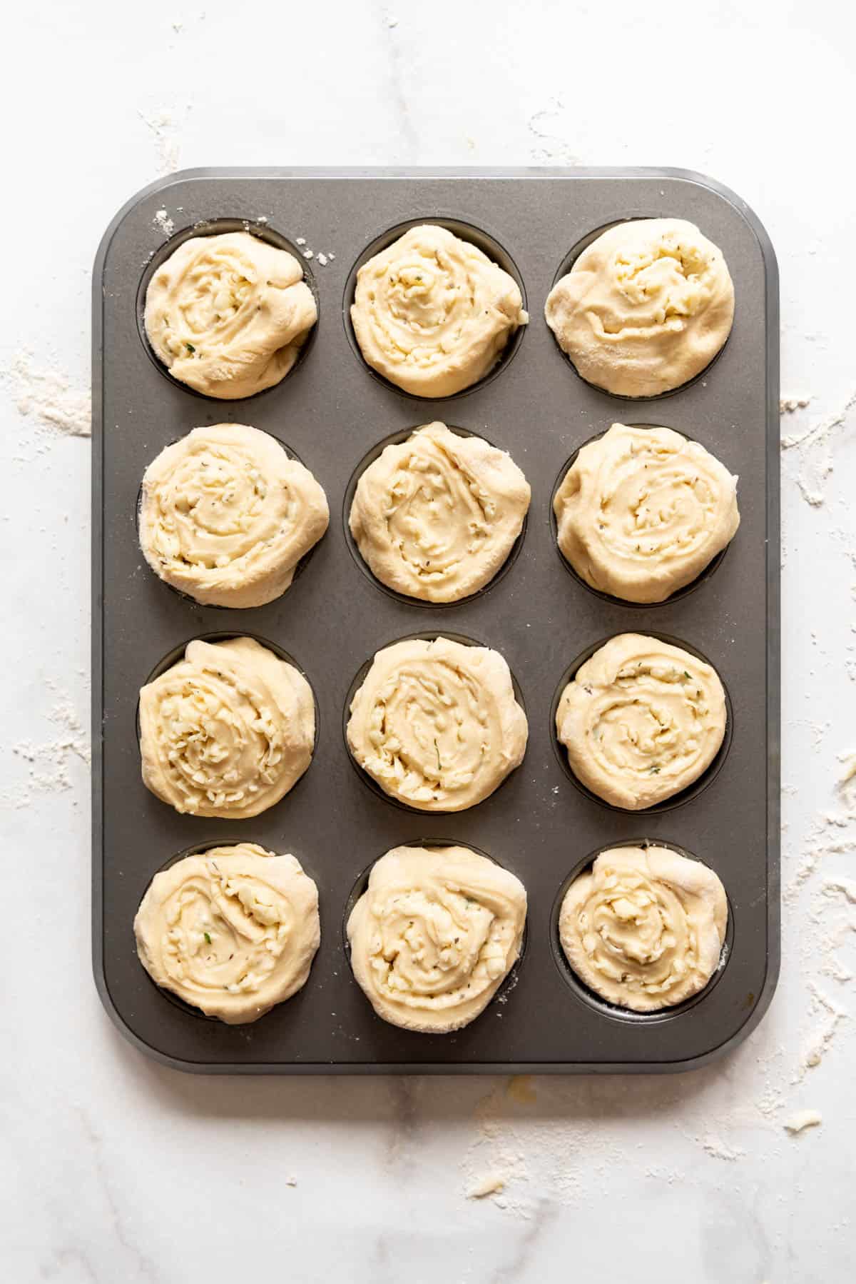 Shaped cheesy garlic mozzarella swirl rolls in a muffin pan before baking.