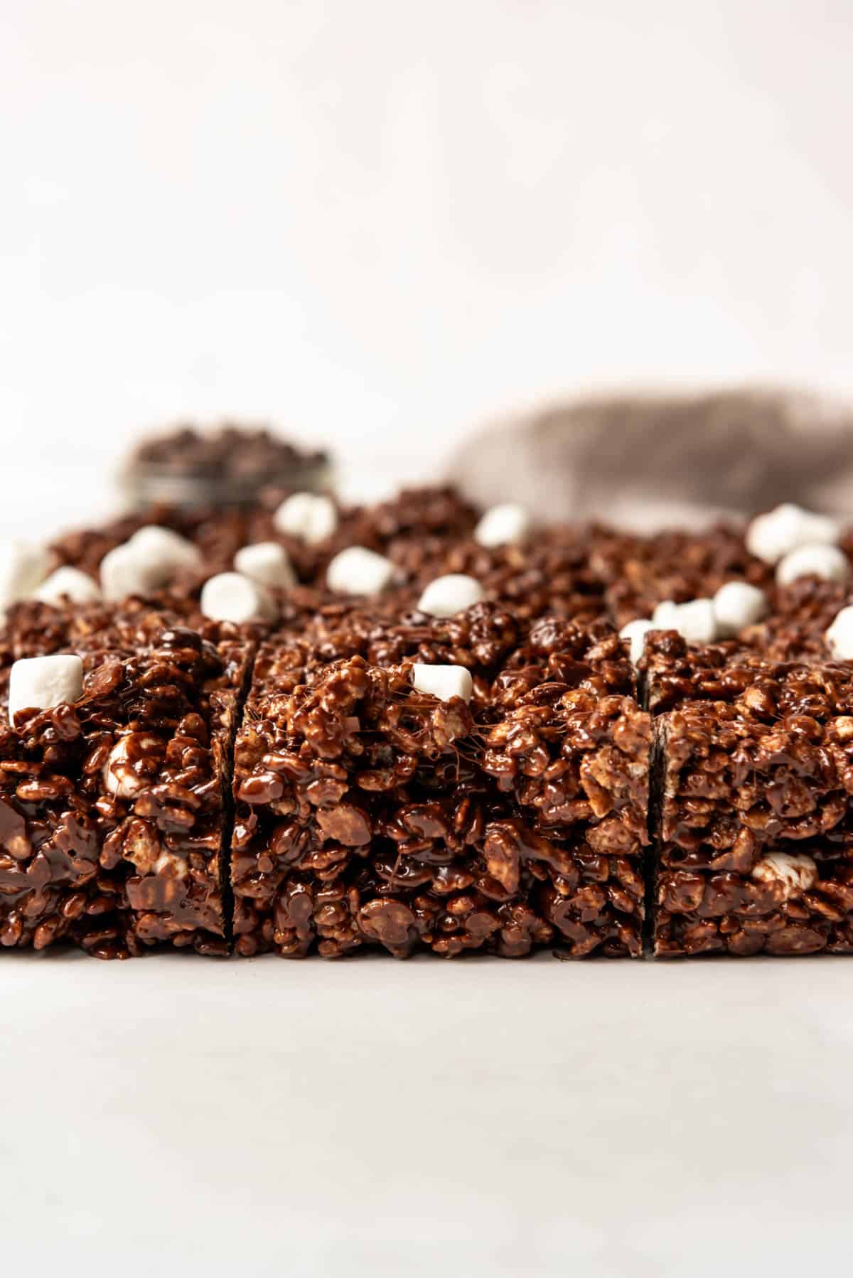 Gooey chocolate rice krispy treats on a white surface with marshmallows on top.