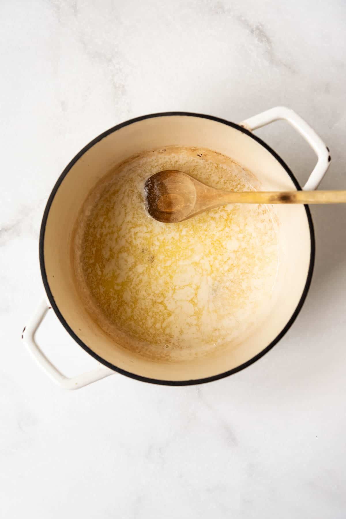 Melting butter in a large pot with a wooden spoon.