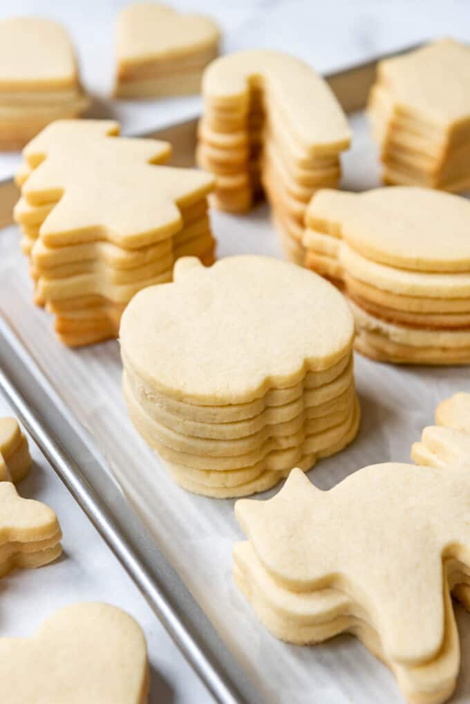 Stacks of unfrosted pumpkin and Christmas tree shaped sugar cookies.