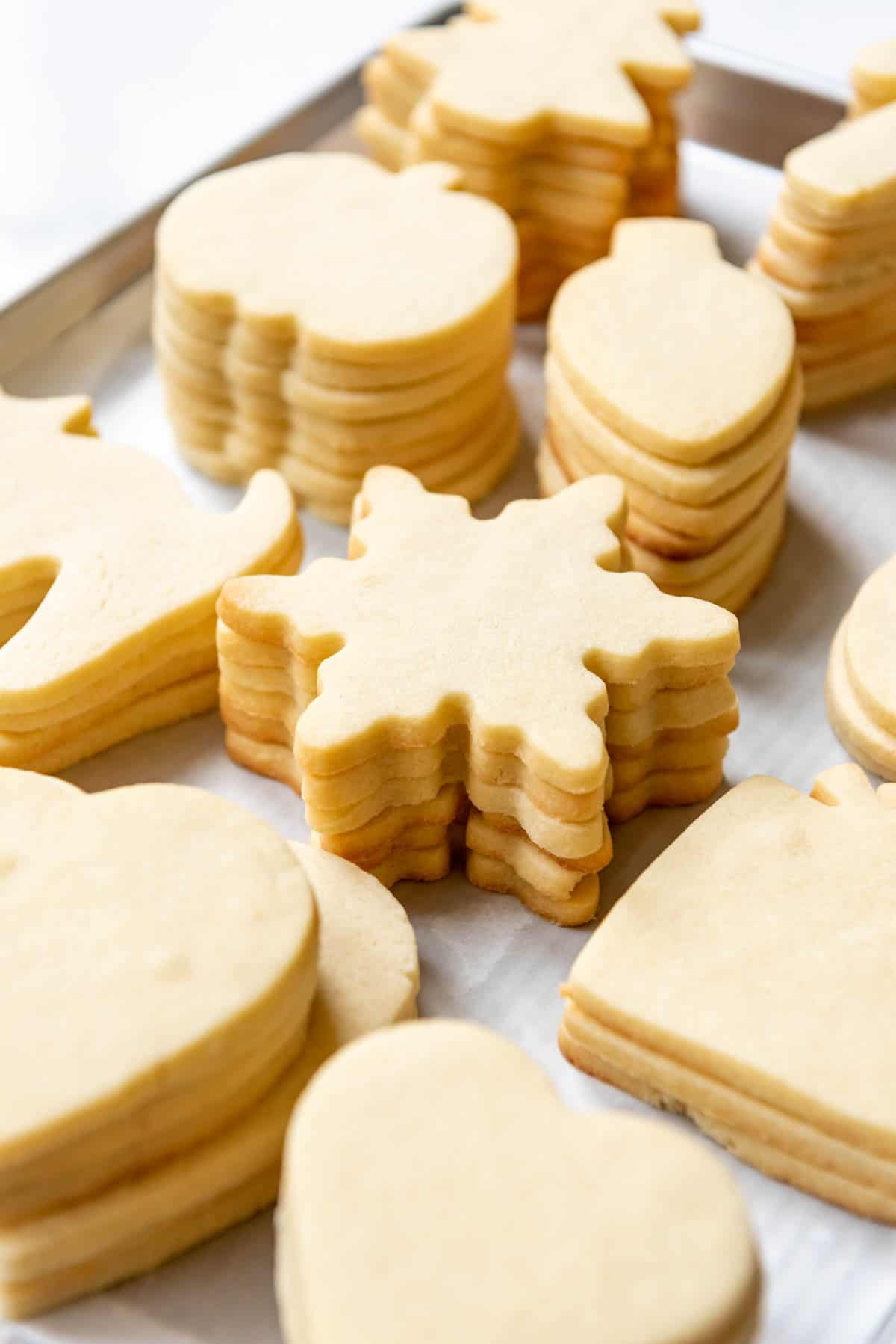 Stacks of cut out sugar cookies in shapes for different holidays on a baking sheet.