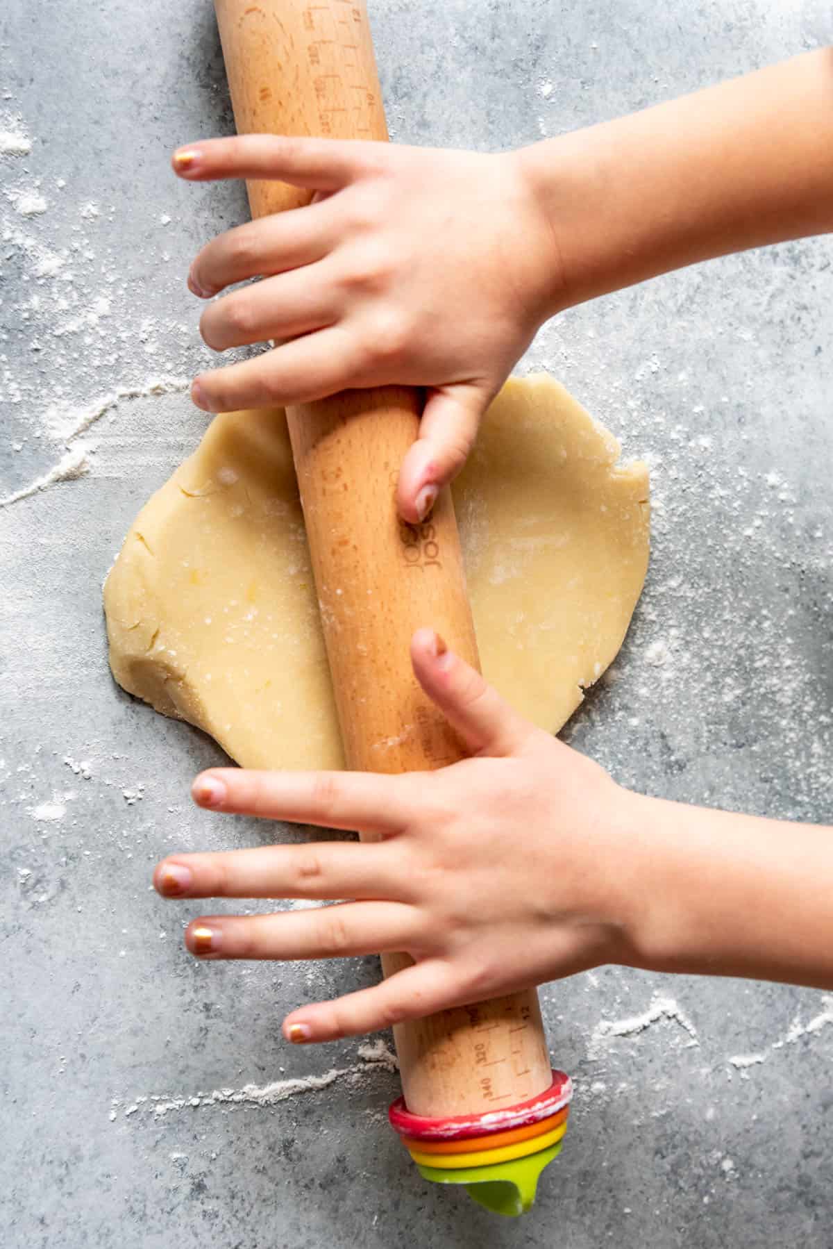 Hands rolling out sugar cookie dough with a wooden rolling pin.