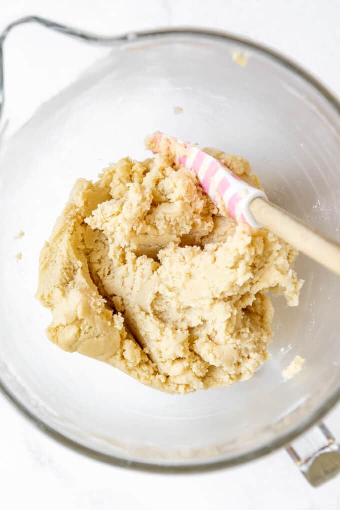 Mixing sugar cookie dough in a large glass mixing bowl.