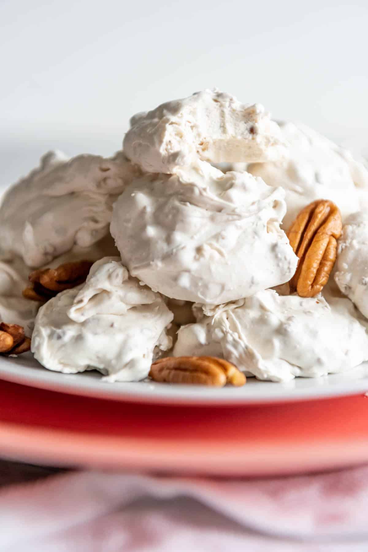 Piled white divinity on a plate with pecans and a bite taken out of the top piece of candy.