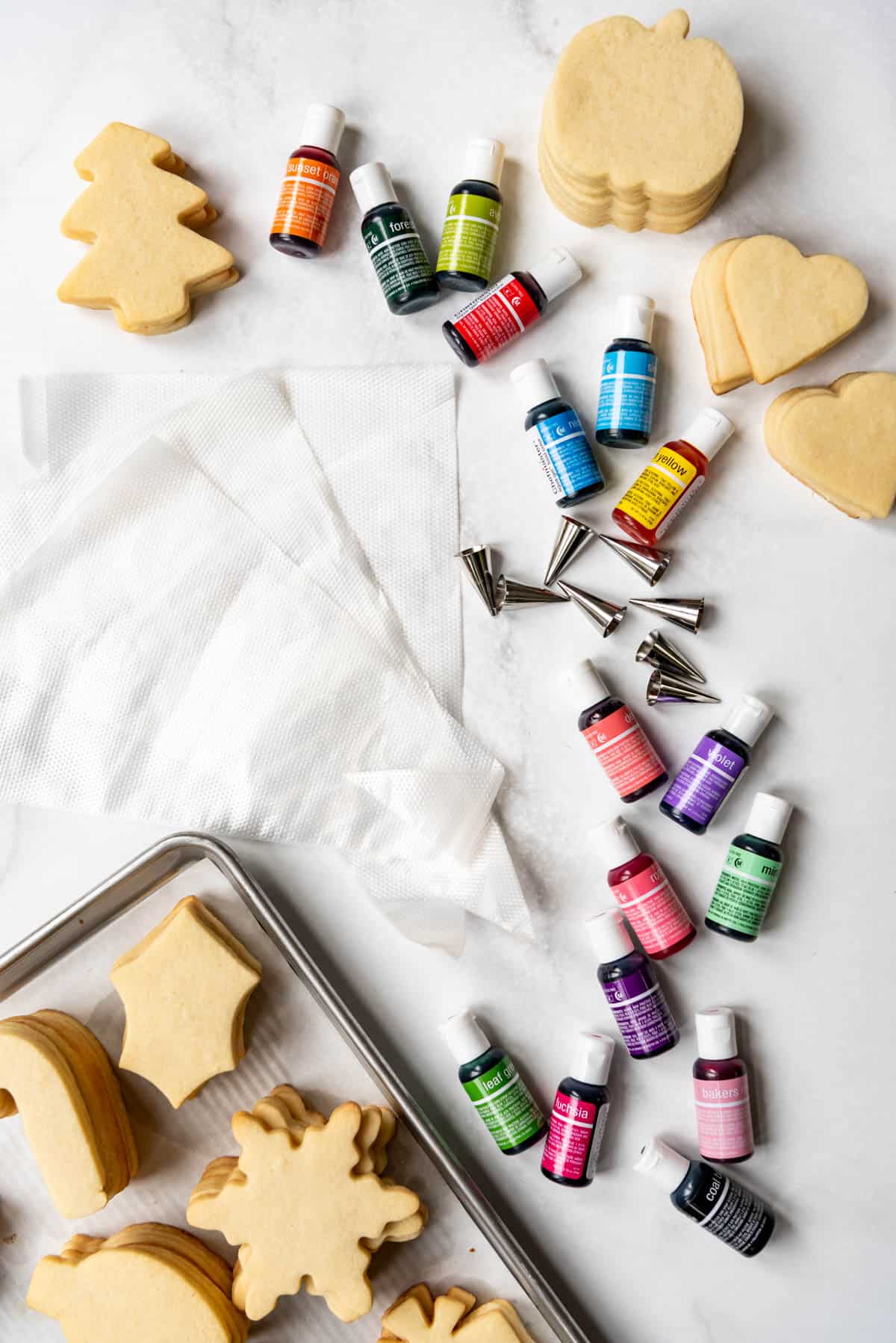 Unfrosted cut out sugar cookies next to bottles of gel food coloring, piping tips, and piping bags.