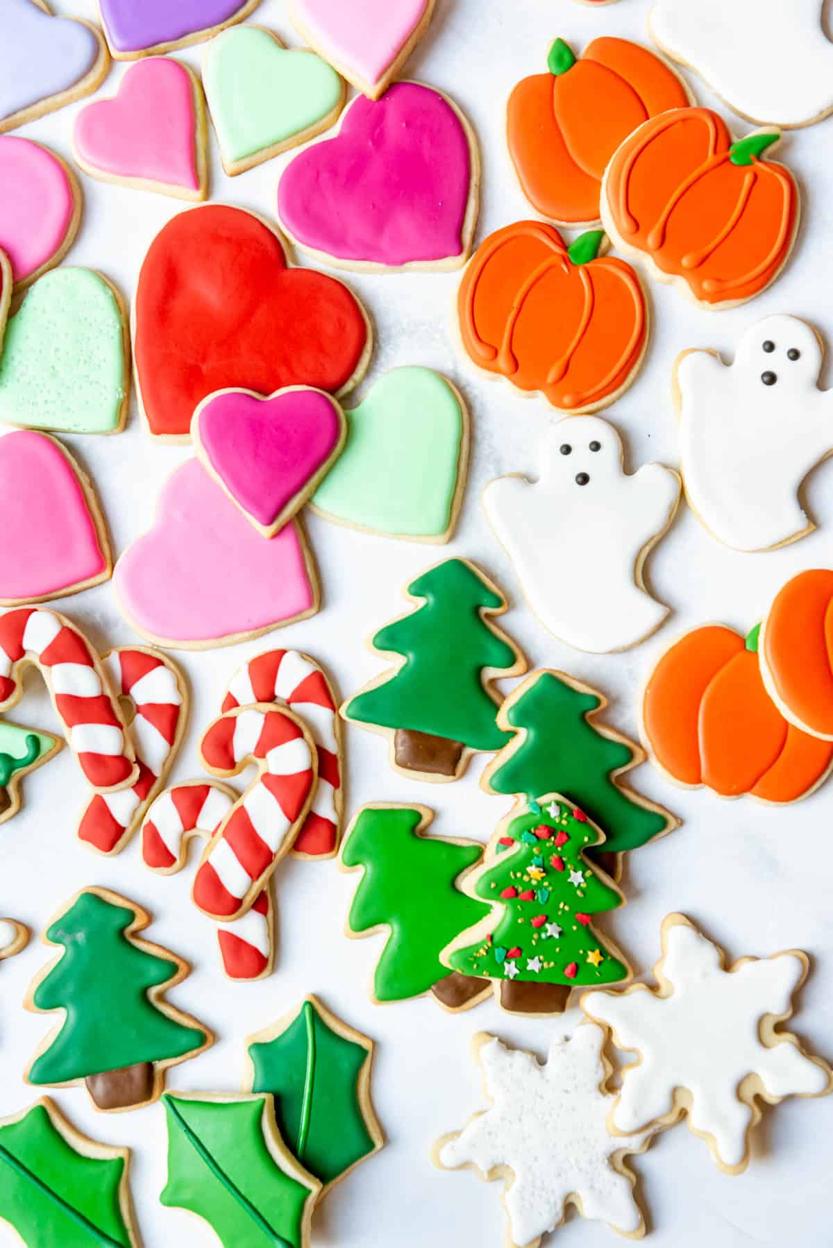 An overhead image of cut out sugar cookies decorated with royal icing in shapes of Christmas trees, candy canes, pumpkins, ghosts, and hearts.