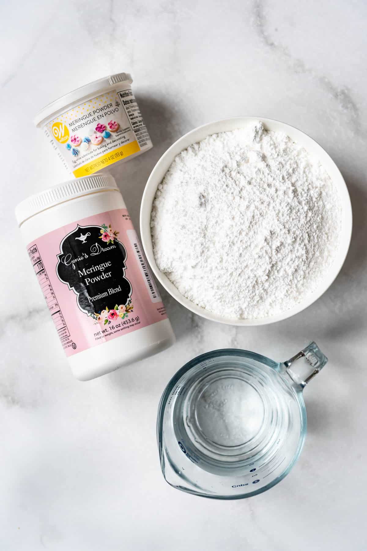 Meringue powder, powdered sugar, and water in bowls on a marble surface.