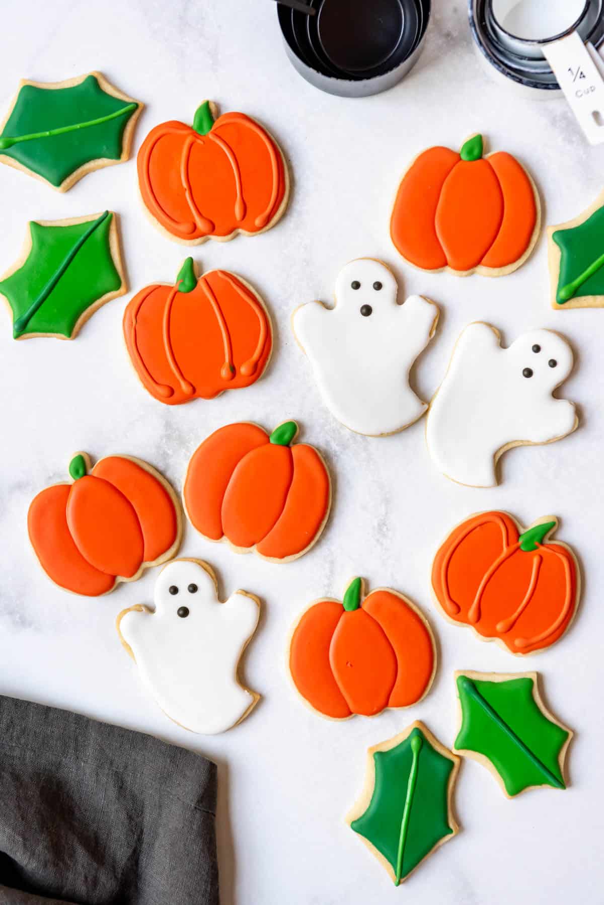 Pumpkin and ghost sugar cookies on a white surface.