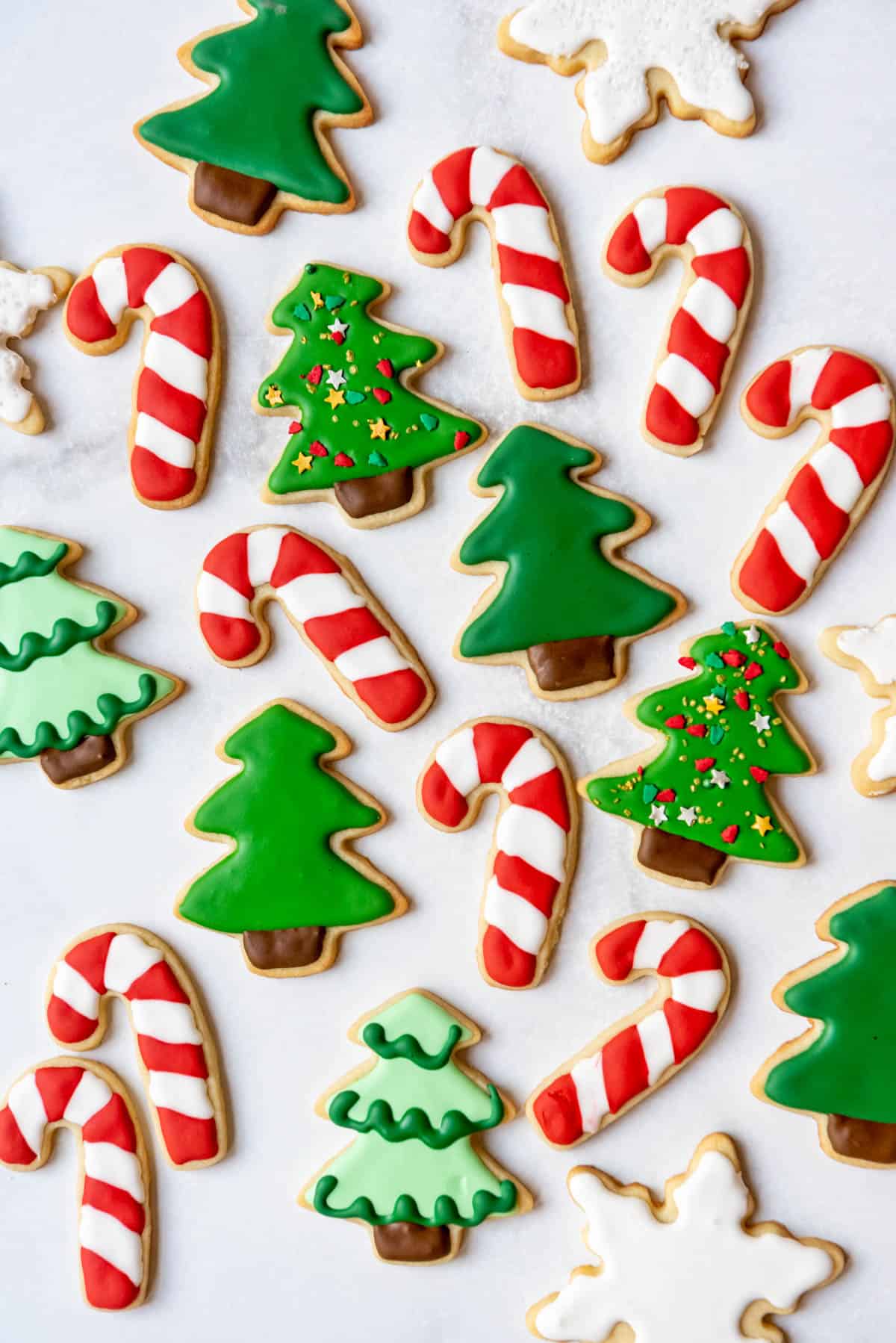 Candy cane and Christmas tree decorated sugar cookies with royal icing and sprinkles.