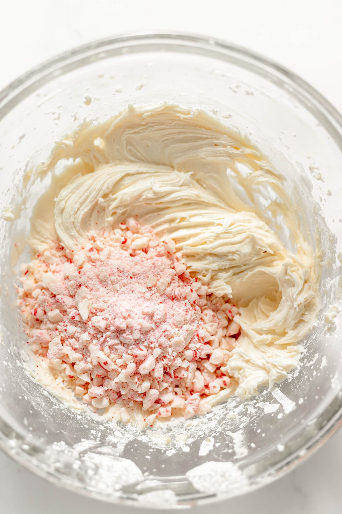 Adding crushed candy canes to frosting in a bowl.
