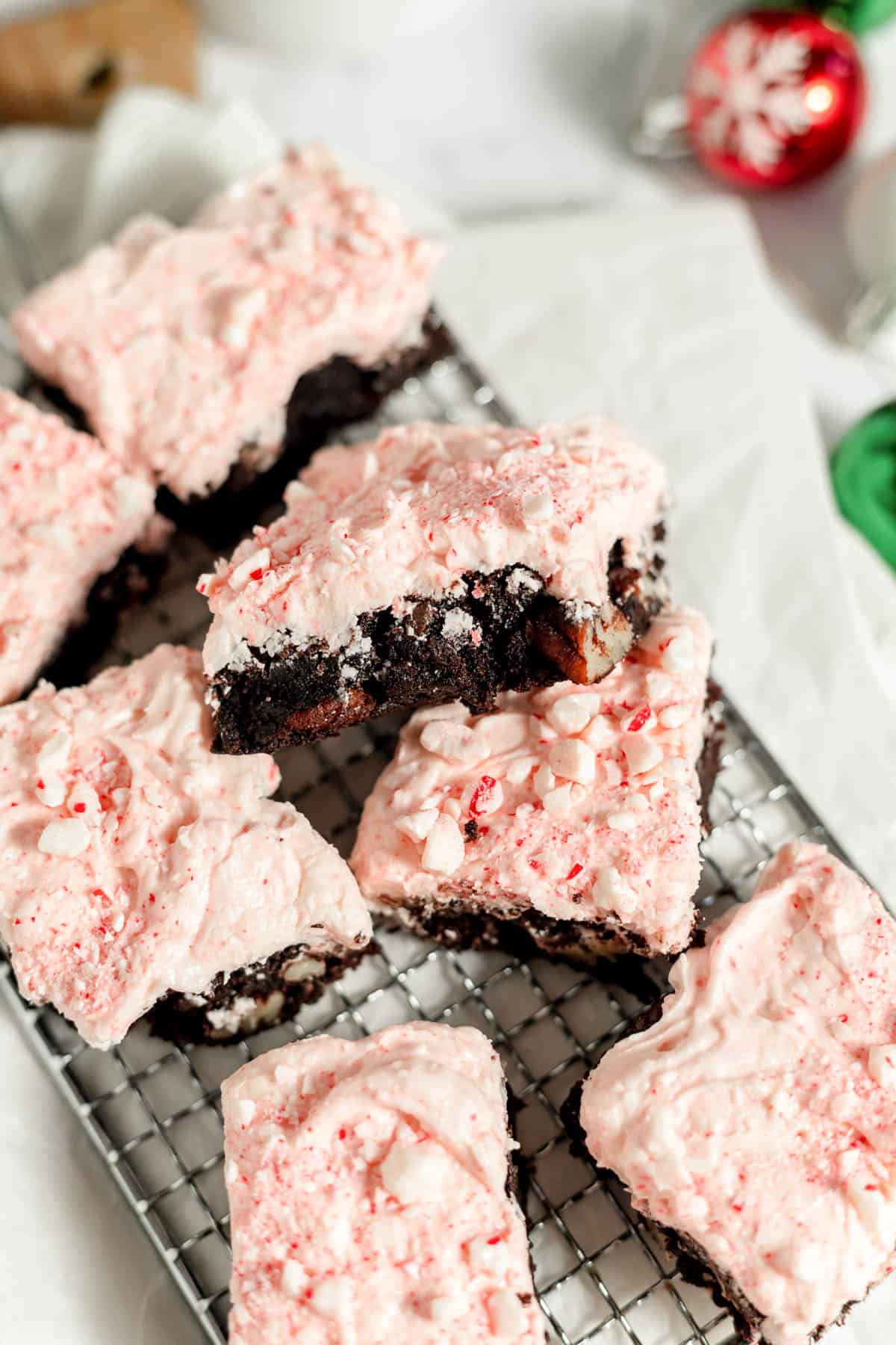 Frosted candy cane brownies haphazardly stacked on a wire rack.
