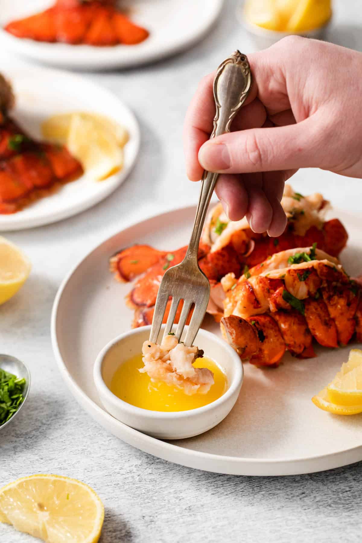 Cooked lobster tail being eaten with a fork, dipped into melted butter in a ramekin. 