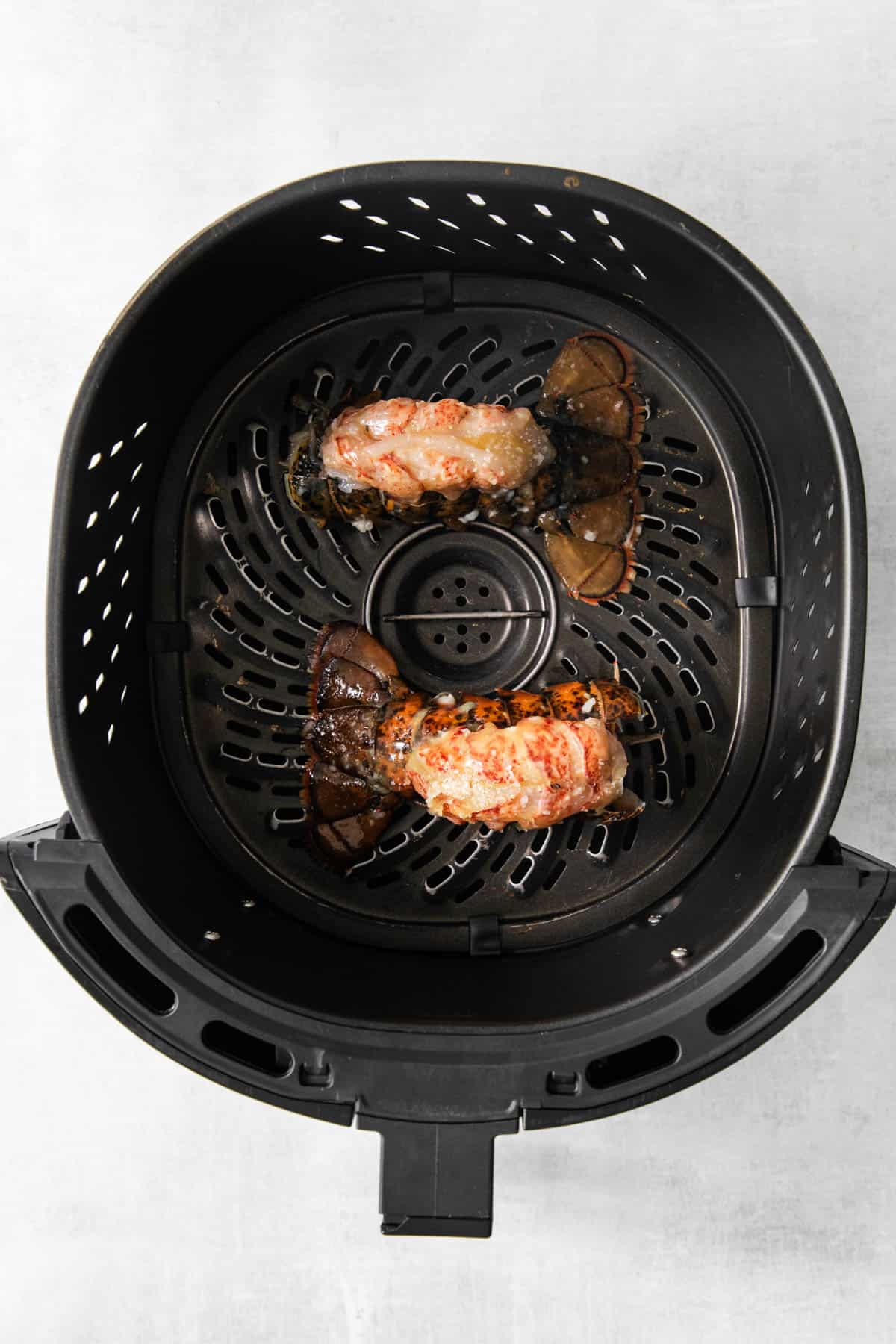 Top view of raw lobster tails in the bottom of an air fryer basket.