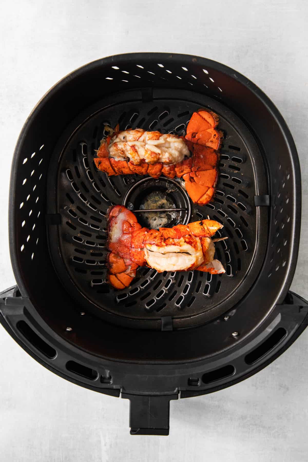 Top view of cooked lobster tails in the bottom of an air fryer basket. 