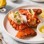 Two lobster tails on a plate with a bowl of melted butter.