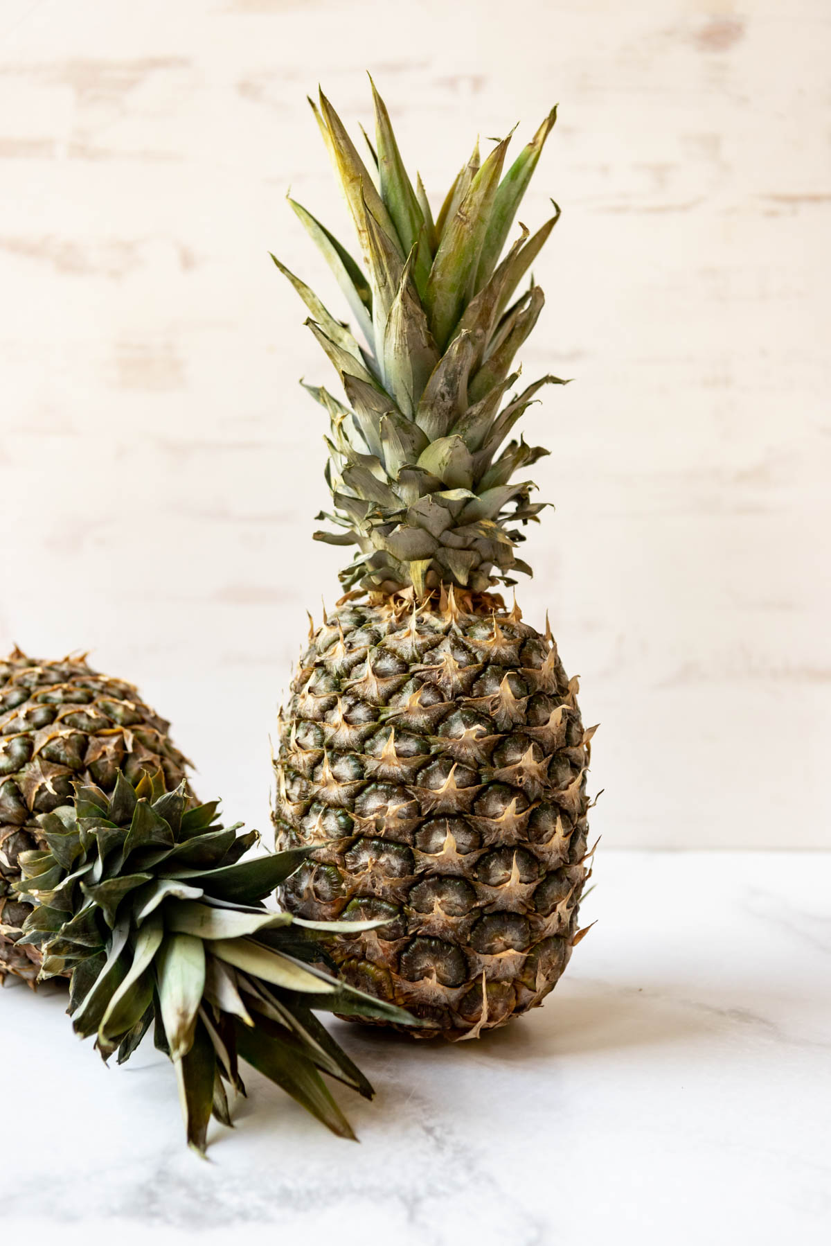 A fresh pineapple standing up on its base with another whole pineapple laying next to it.