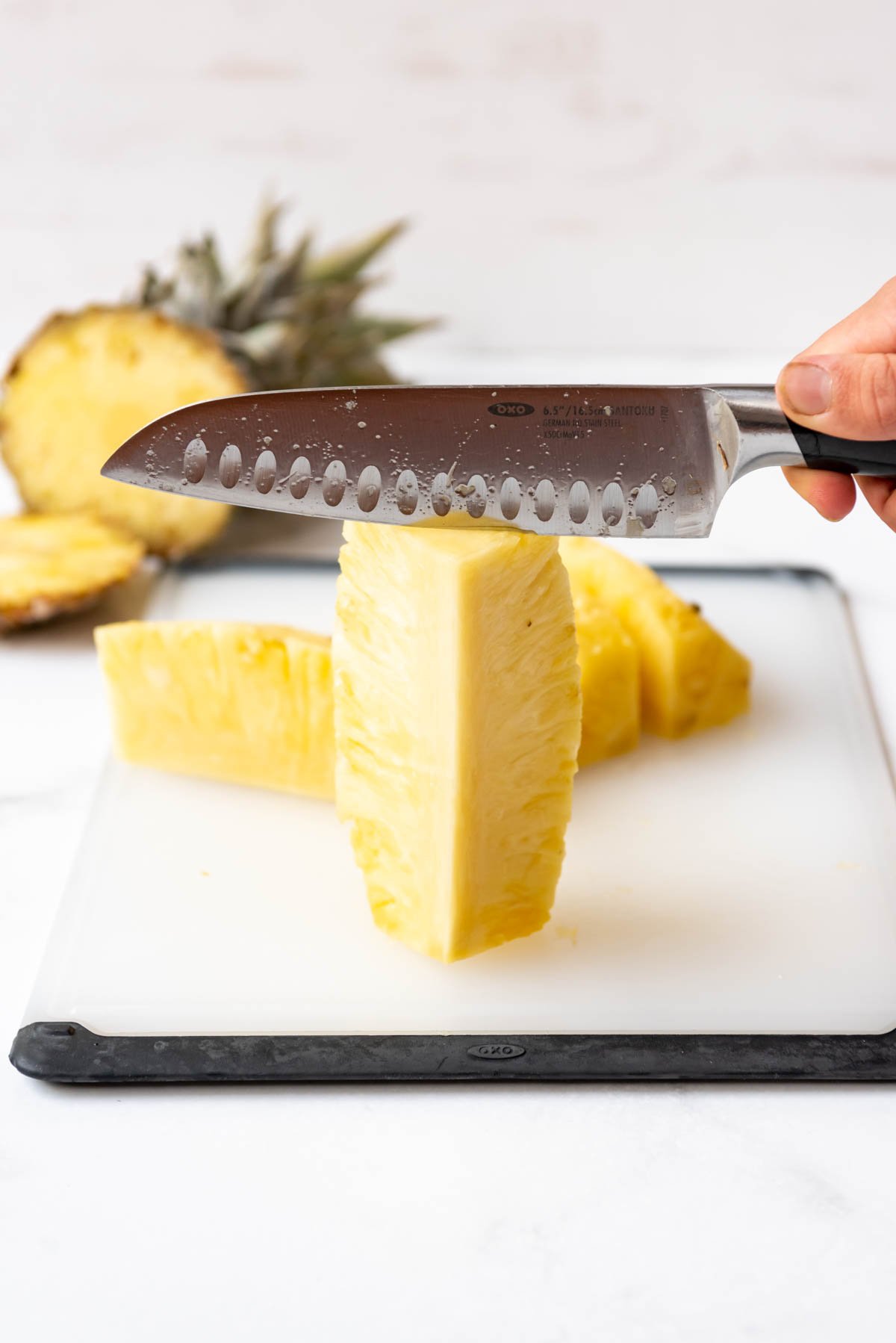 A piece of pineapple standing on end on a cutting board with a knife being used to cut off the core.
