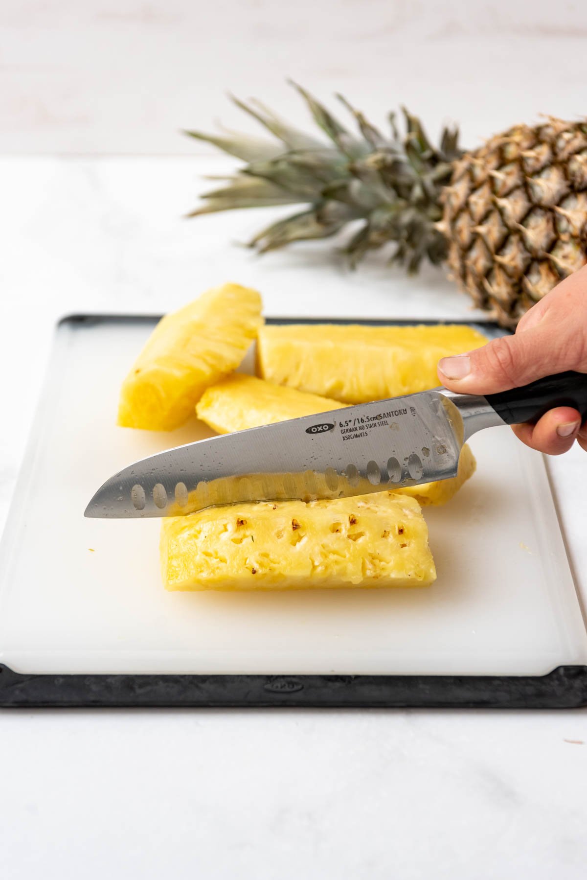 A knife being used to cut pineapple into spears.