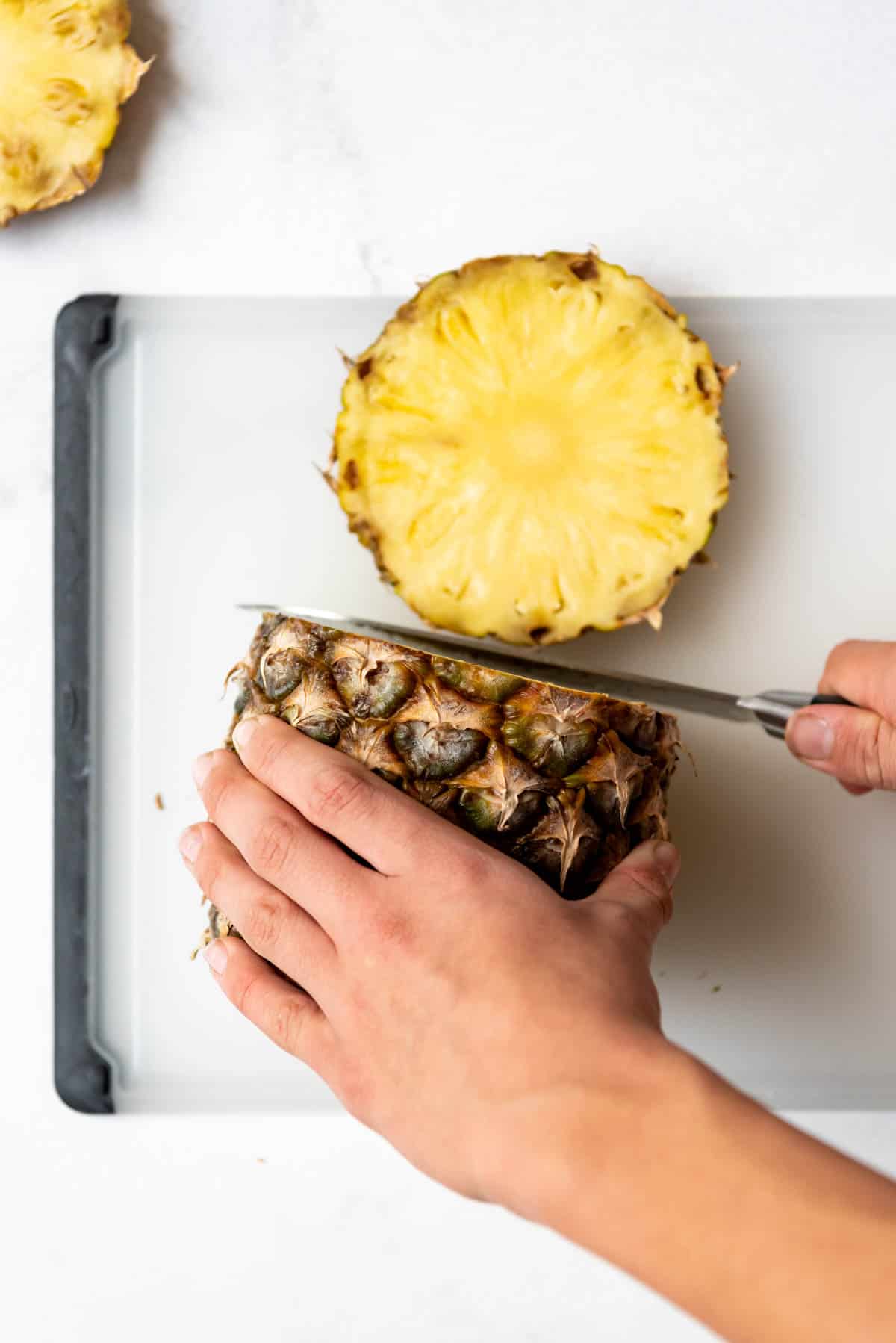 A hand holding a pineapple and knife to slice pineapple rings.