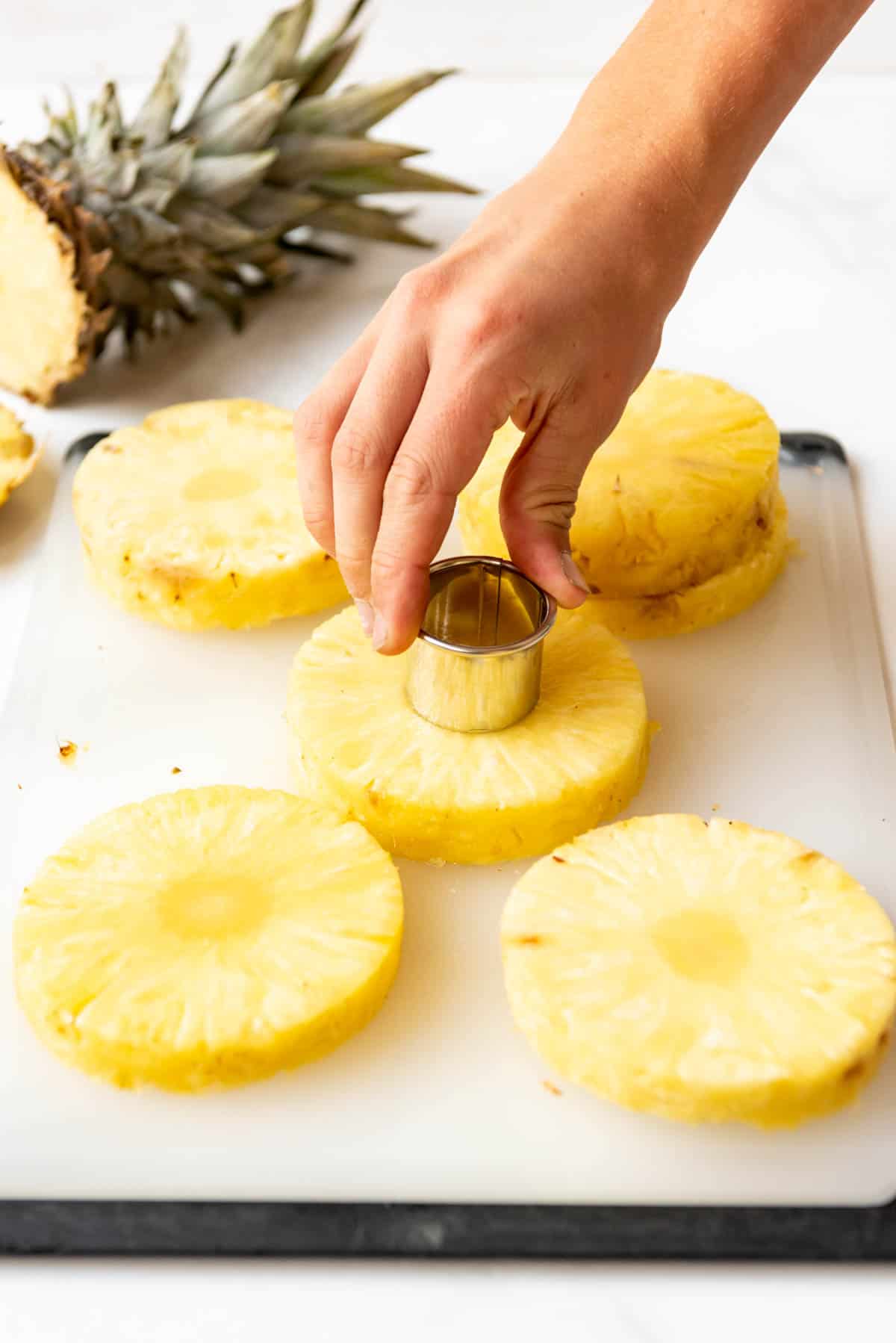 A hand holding a small circular metal cutter to remove the core from slices of fresh pineapple.
