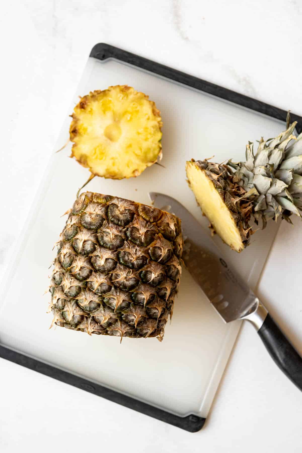 A pineapple with the crown and bottom sliced off on a cutting board.