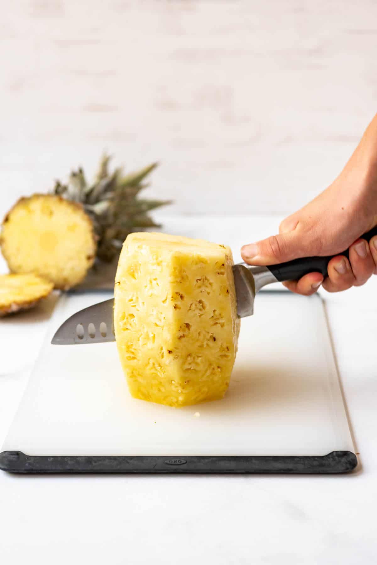 A knife being used to cut a pineapple in half.
