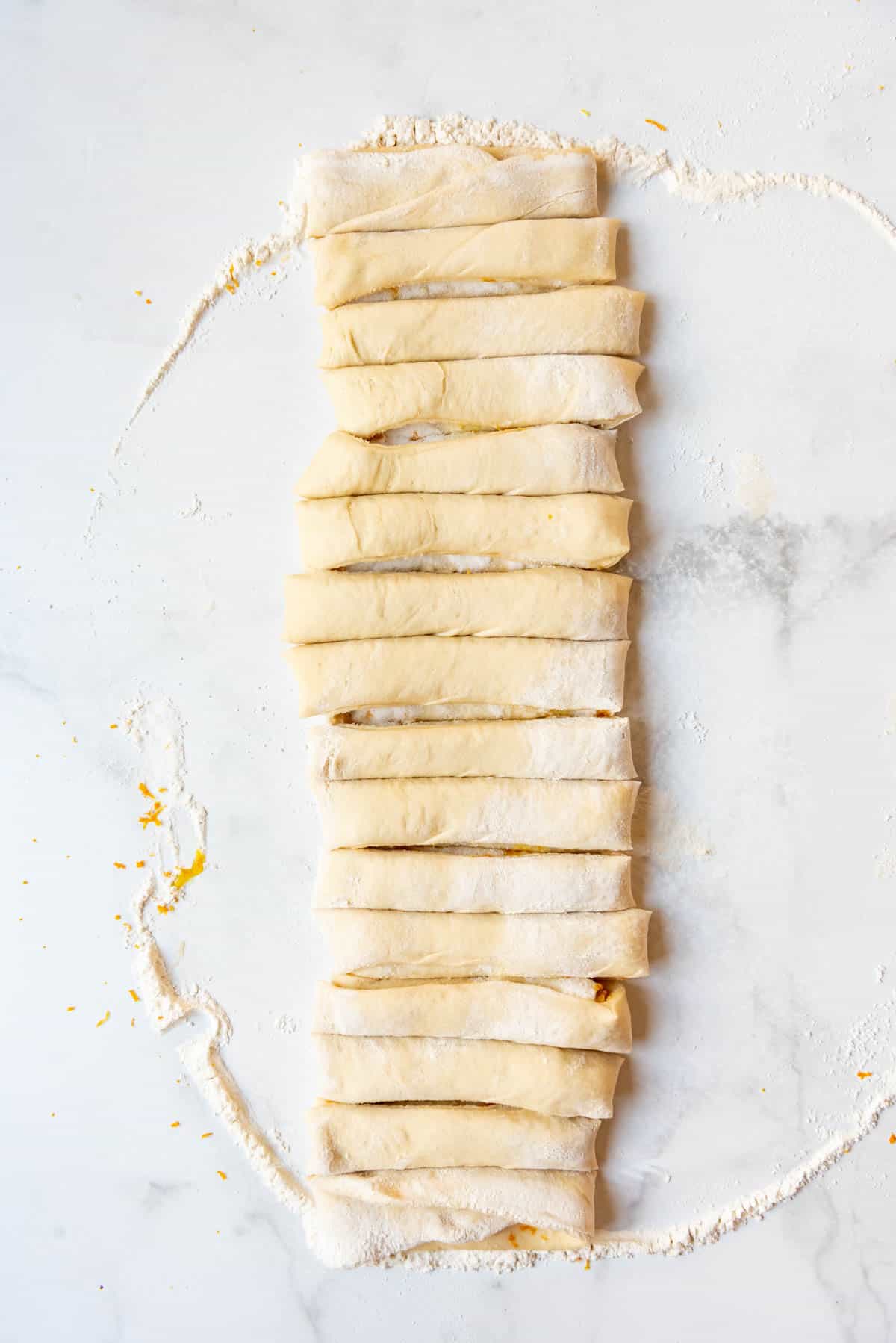 Folded sweet roll dough cut into strips on a white surface.