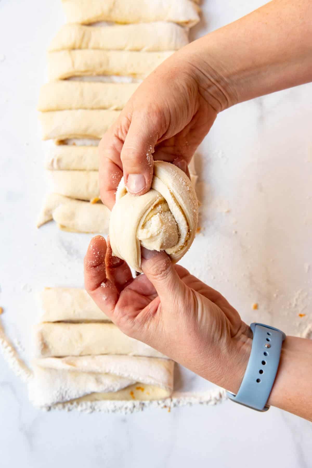 Pushing one end of dough through a loop to make a knotted orange sweet roll.