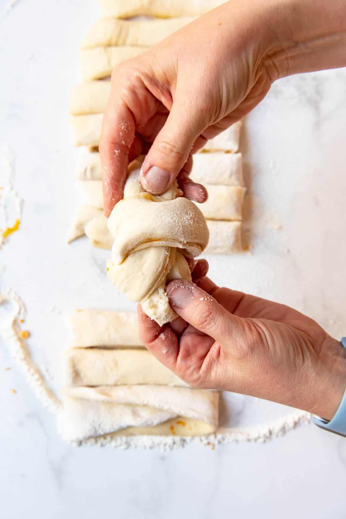 Gently tugging on the ends of a knotted sweet roll dough.