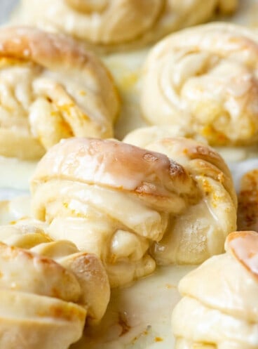 A close images of glazed knotted orange sweet rolls.