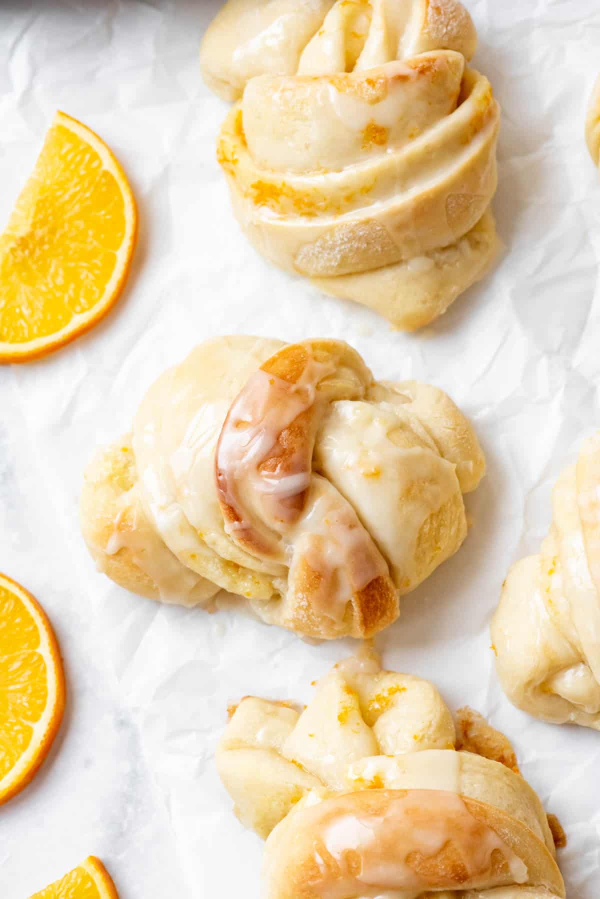 An overhead image of a knotted orange sweet roll on parchment paper next to more rolls.