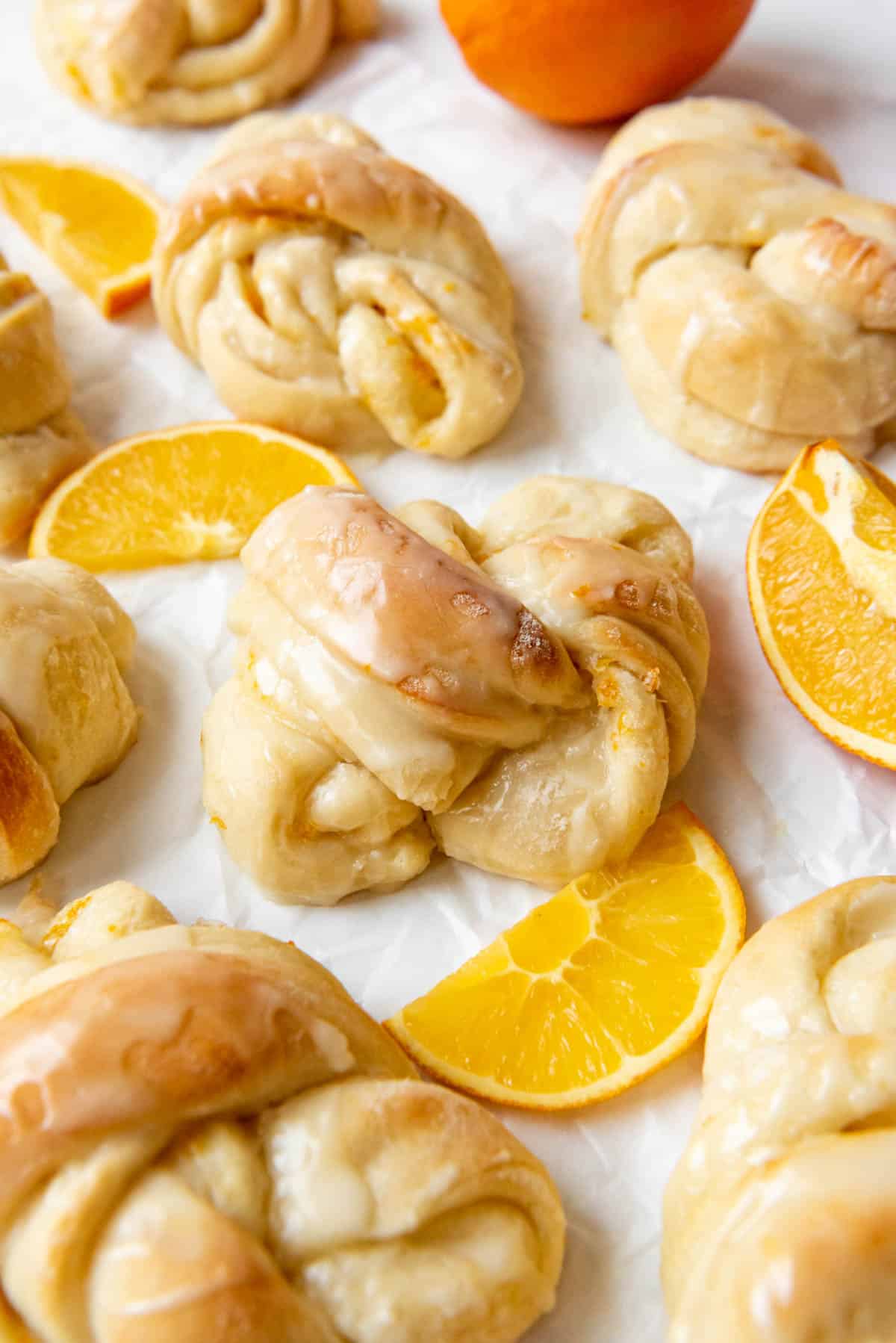 A knotted orange sweet roll on a white surface next to orange slices.