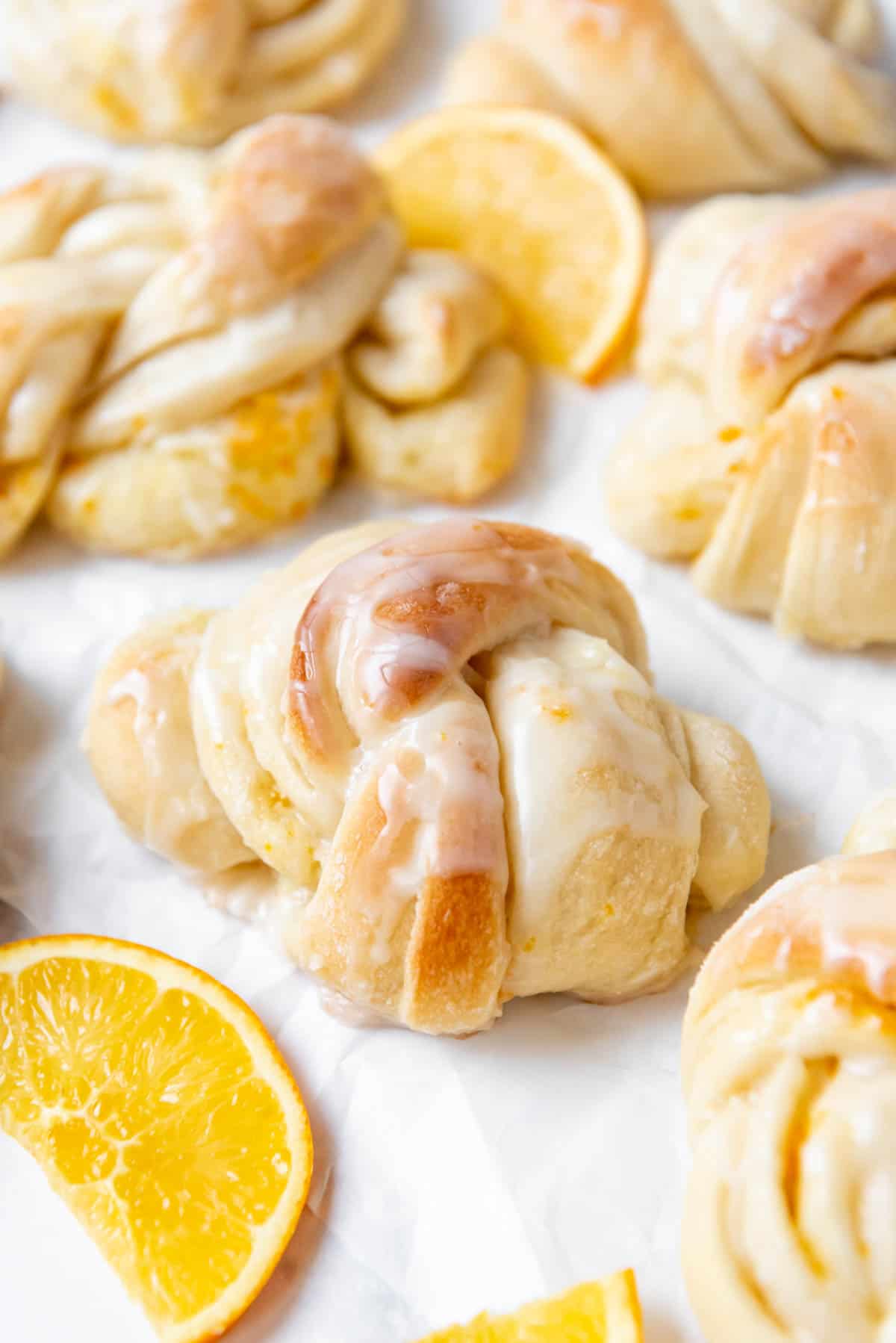 An image of knotted orange sweet rolls next to orange slices.