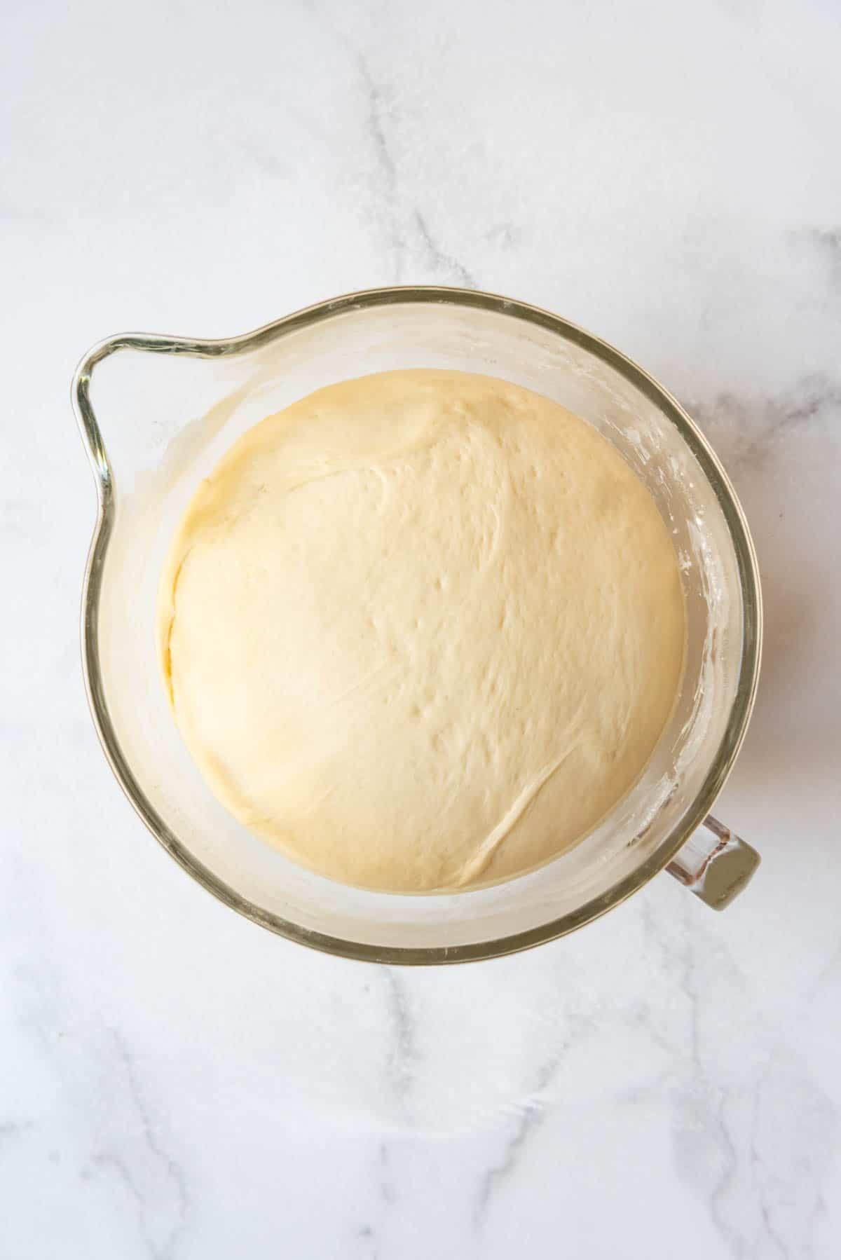 Risen orange sweet roll dough that has doubled in size in a glass bowl.
