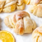 An image of knotted orange sweet rolls next to orange slices.