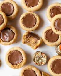 Peanut Butter Cup Cookies with a bite taken out of one of them and some wrapped mini Reese's peanut butter cups scattered around them.