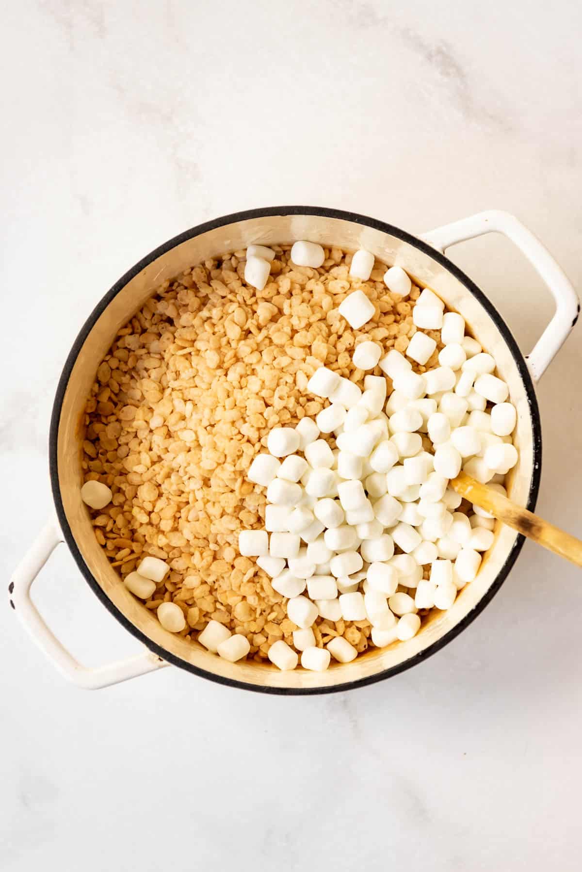 Top view of a dutch oven with rice krispies and marshmallows in it with a wooden spoon. 