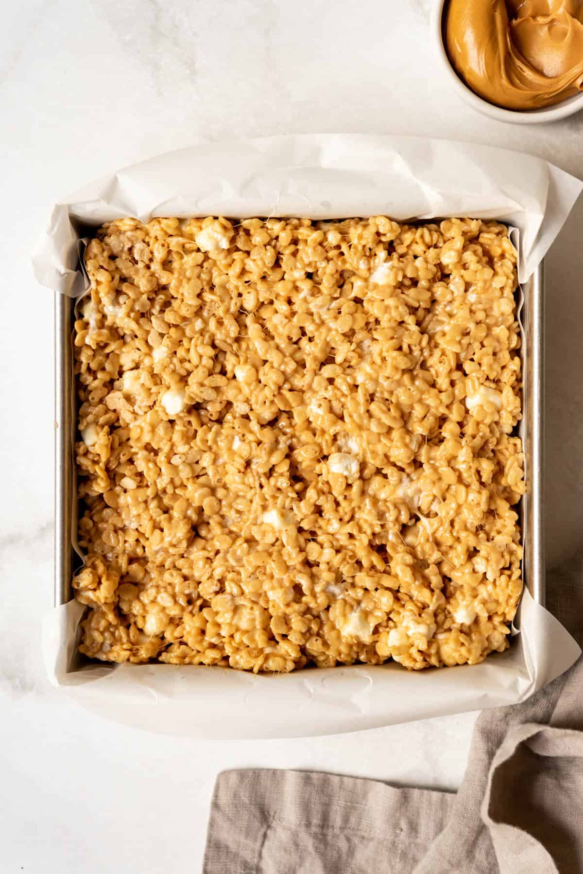 Top view of a square pan with peanut butter rice krispie mixture in it. 