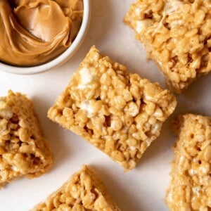 Peanut butter rice krispie treat squares next to a bowl of creamy peanut butter.