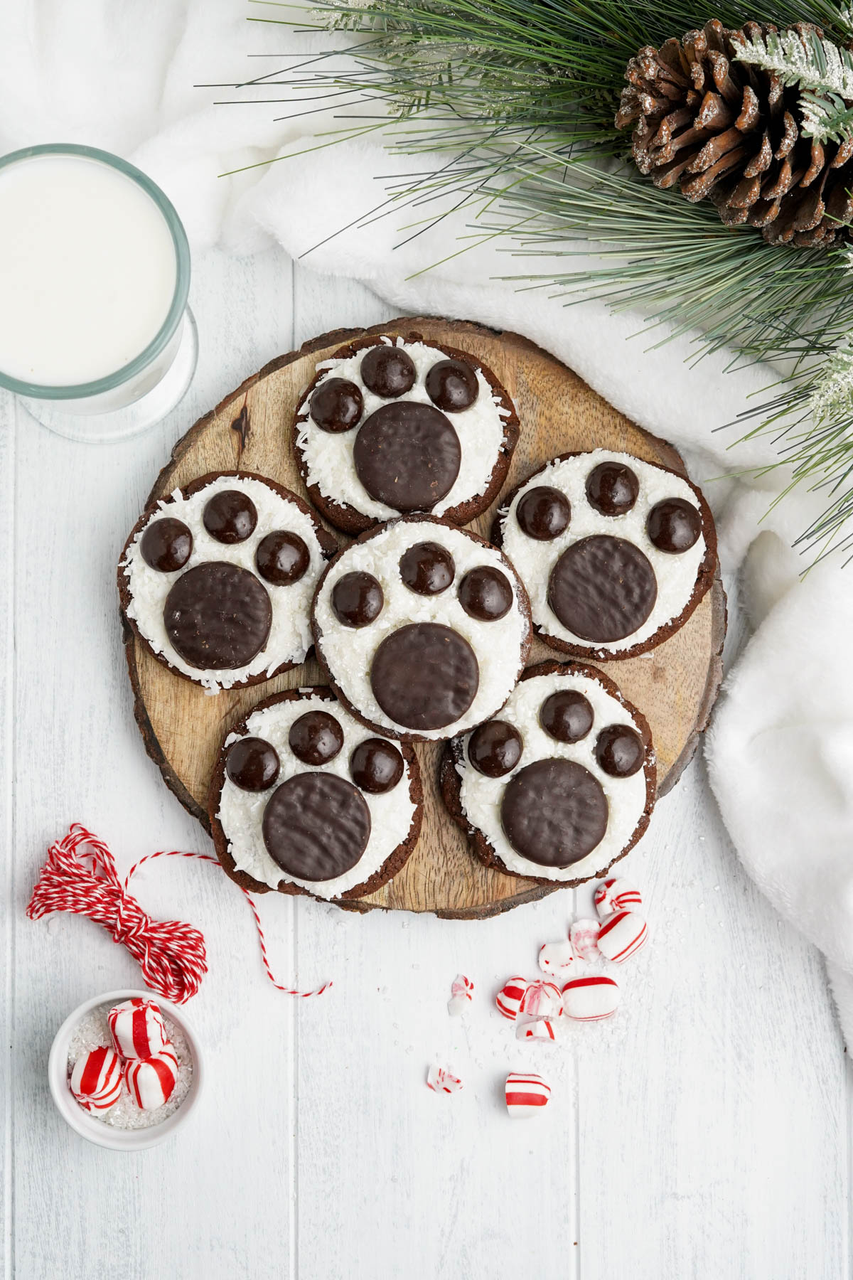An overhead image of frosted chocolate polar bear paw print cookies with crushed peppermint pieces and greenery beside them.