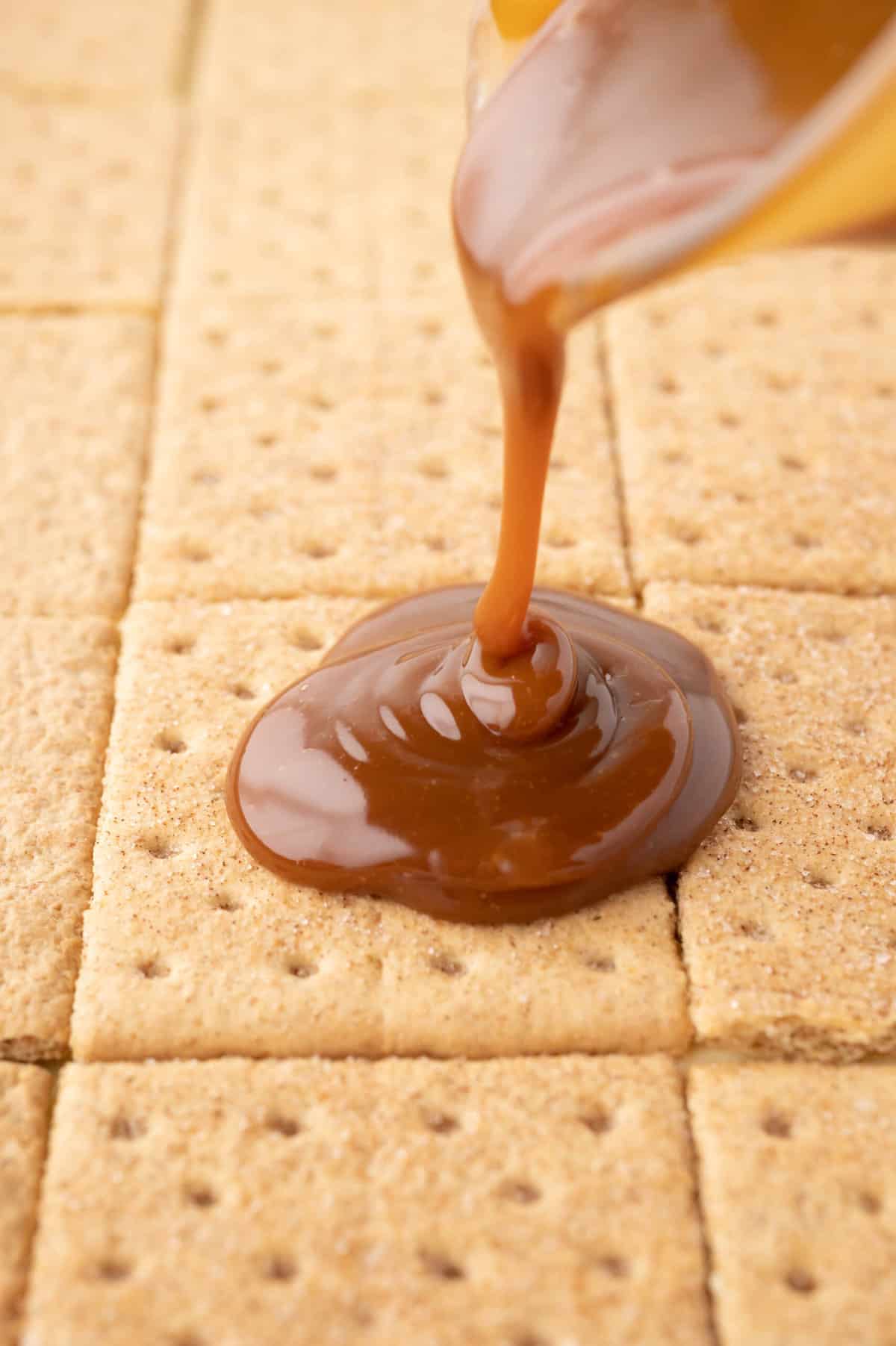 Pouring caramel topping onto a layer of graham crackers.