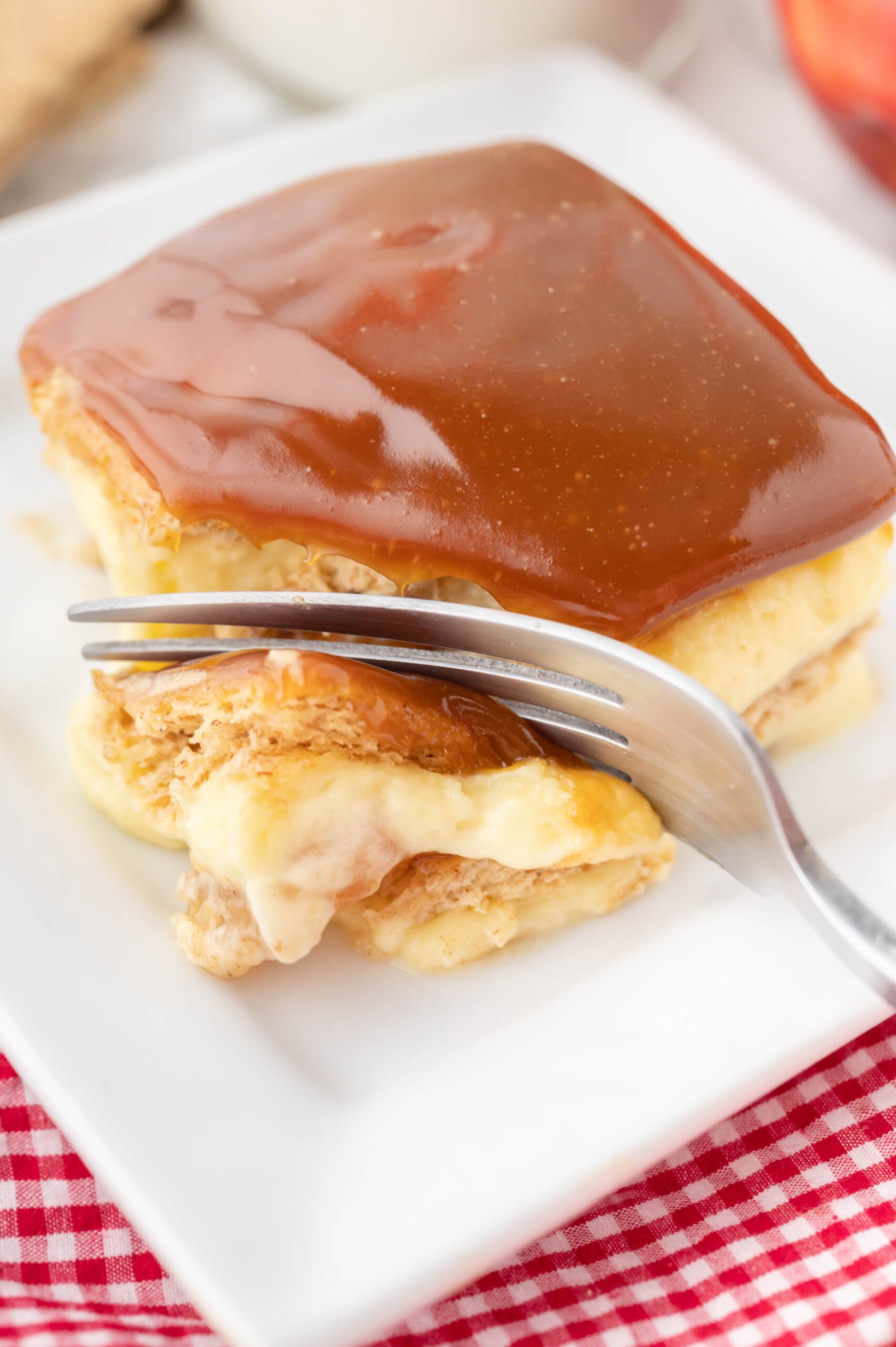 A fork cutting a bite from a slice of caramel apple eclair cake on a white plate.