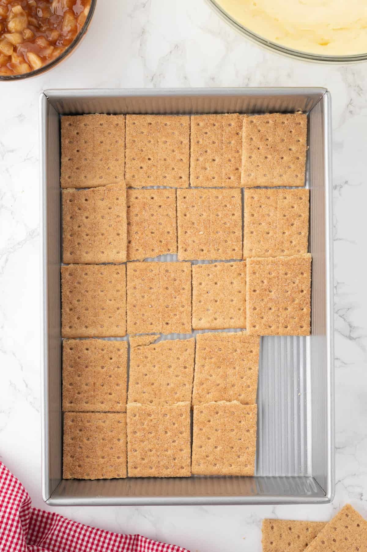 Cinnamon graham cracker squares arranged in a single layer on the bottom of a 9x13-inch baking pan.