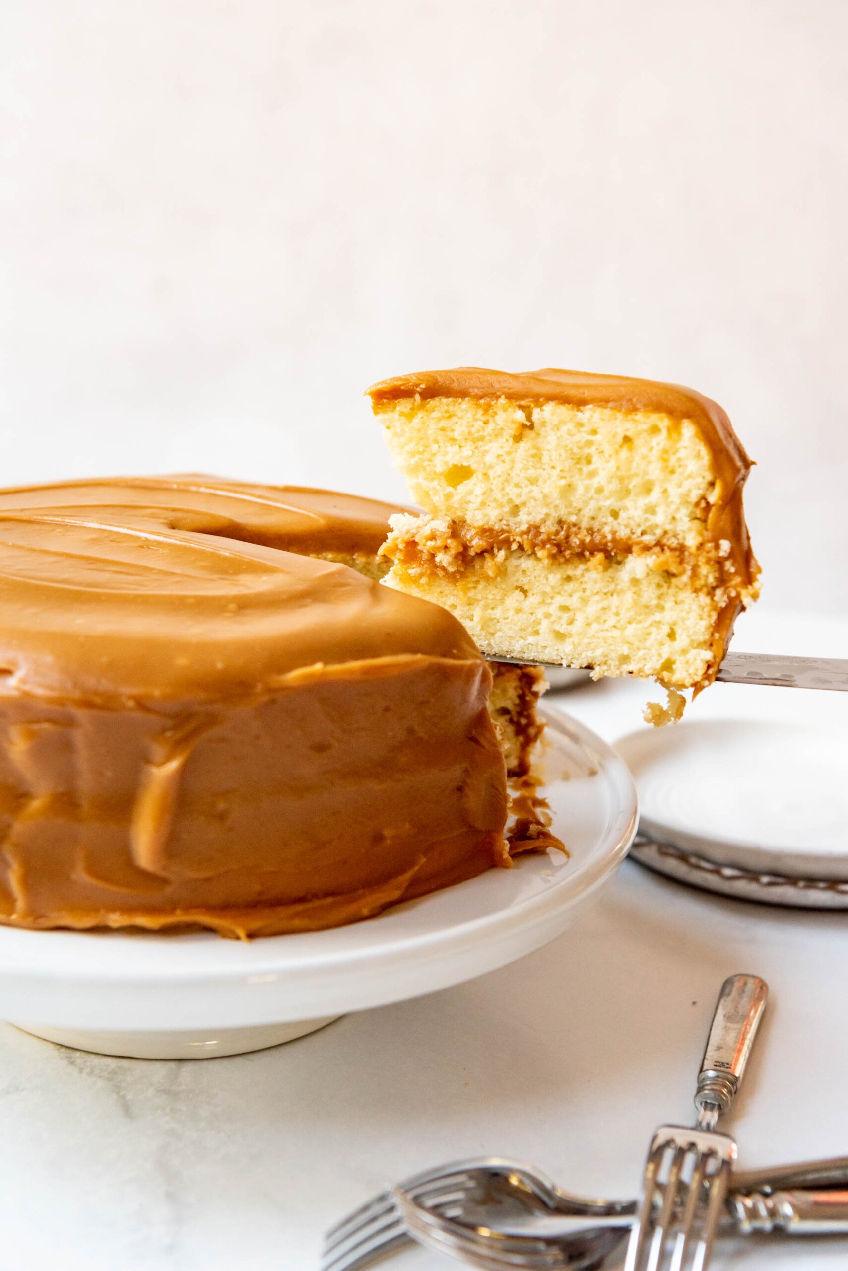 A slice of caramel cake being lifted from the cake plate.
