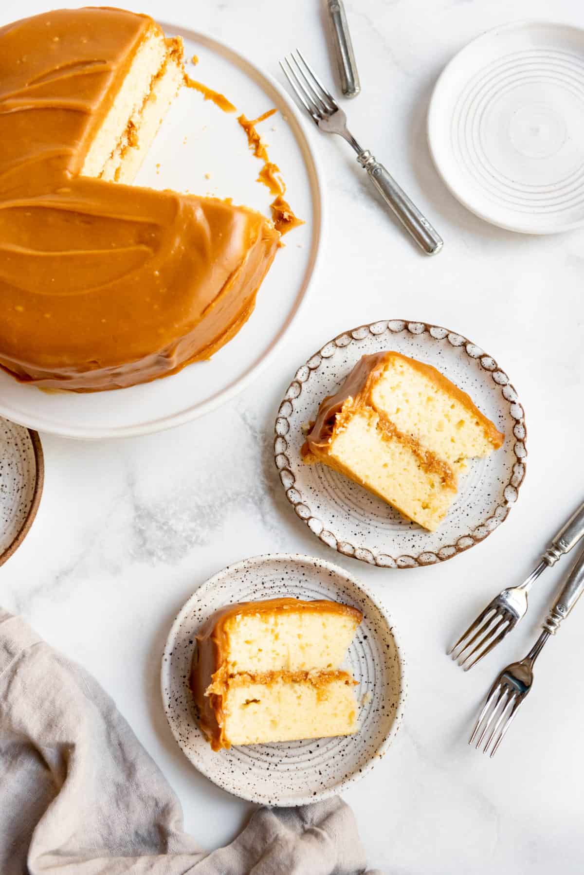 Slices of homemade caramel cake on plates next to the rest of the cake on a cake stand.